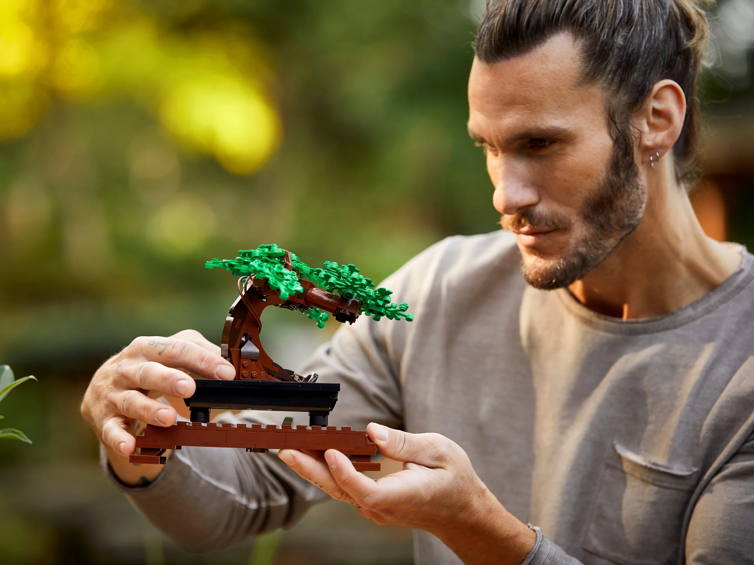 Un bărbat admiră un bonsai LEGO, ținându-l în mâini cu atenție.