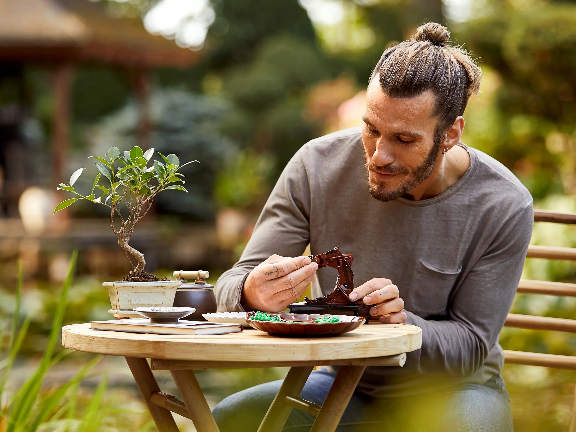 Un bărbat construiește bonsai-ul LEGO, într-un cadru relaxant de grădină. O activitate pașnică.