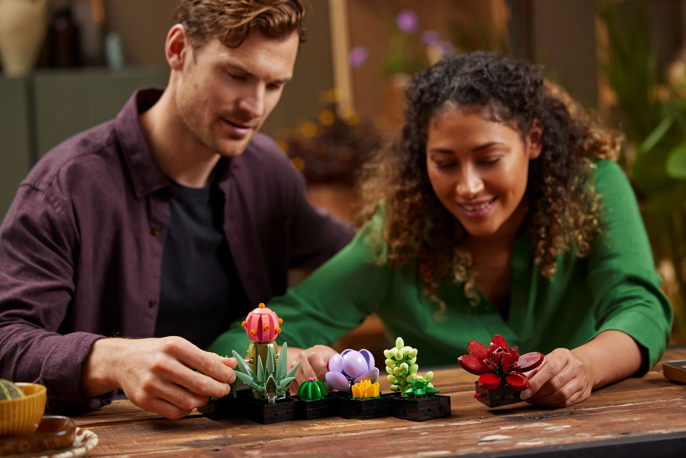 Un cuplu construiește împreună setul LEGO Succulents, zâmbind și concentrându-se.