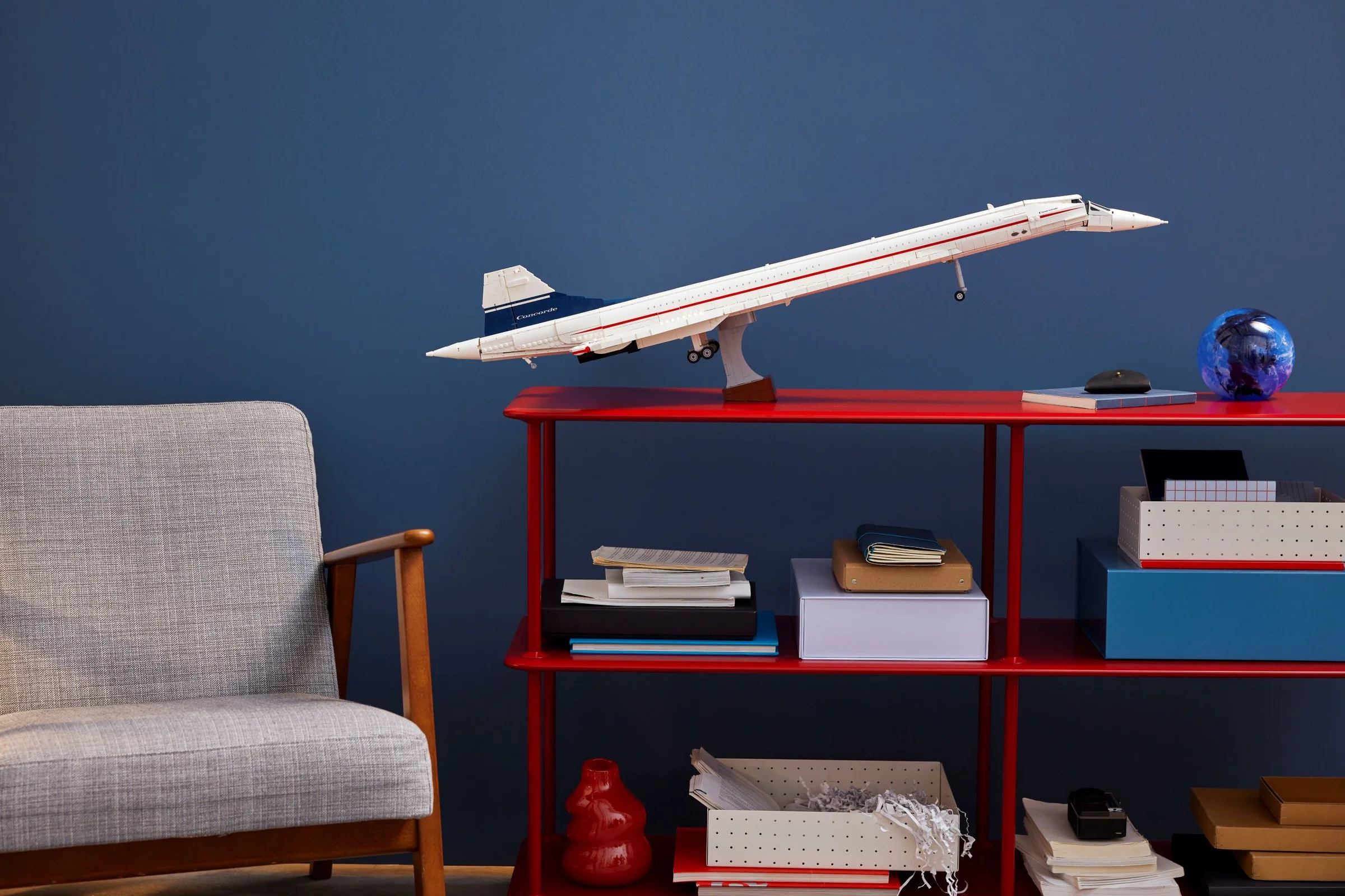 Modelul LEGO Concorde 10318 pe un raft roșu, într-un decor de birou modern.