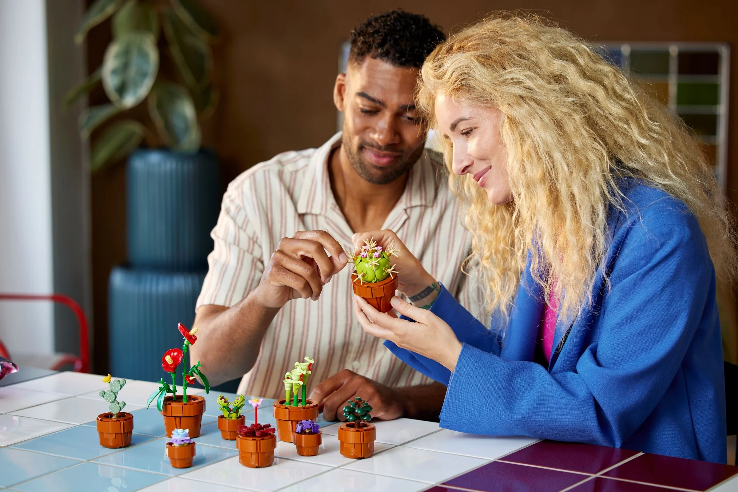 Cuplu asamblând setul LEGO cu plante mici, zâmbitori. O activitate relaxantă împreună.