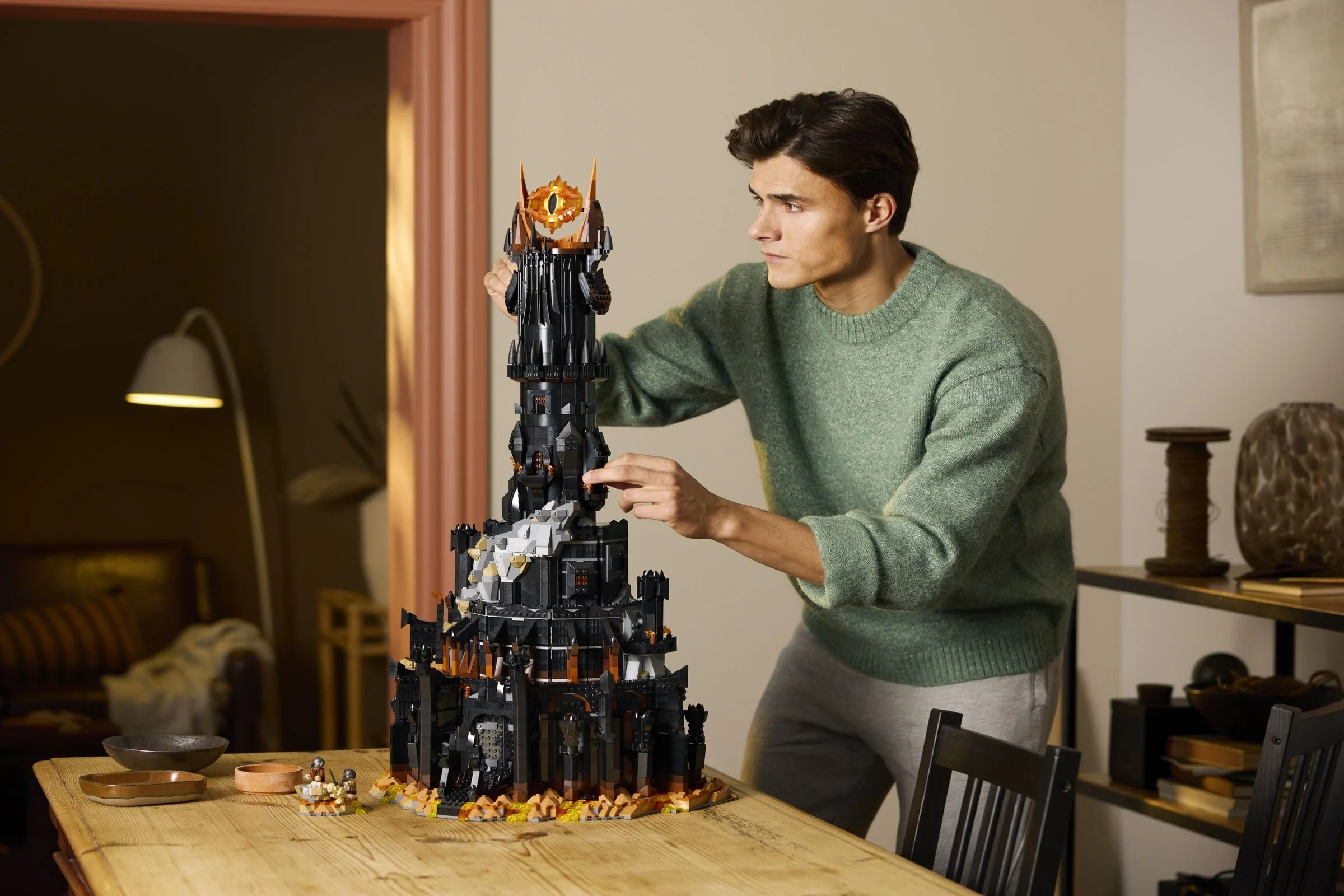Bărbat construind Barad-dûr LEGO. Modelul masiv domină masa de lemn.