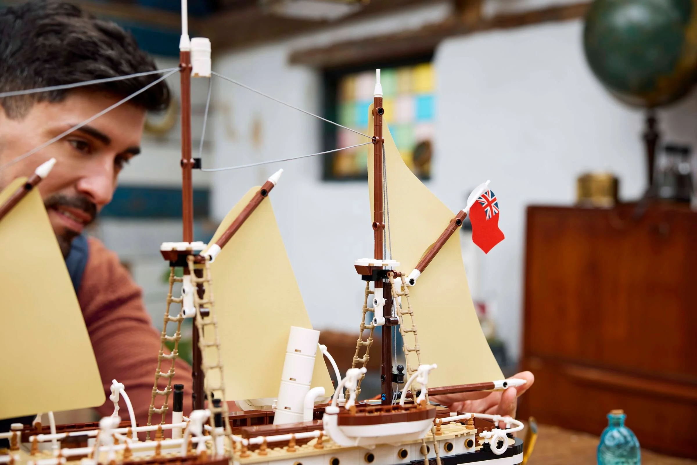 Un bărbat construiește corabia Endurance LEGO, cu vele și catarg vizibile.