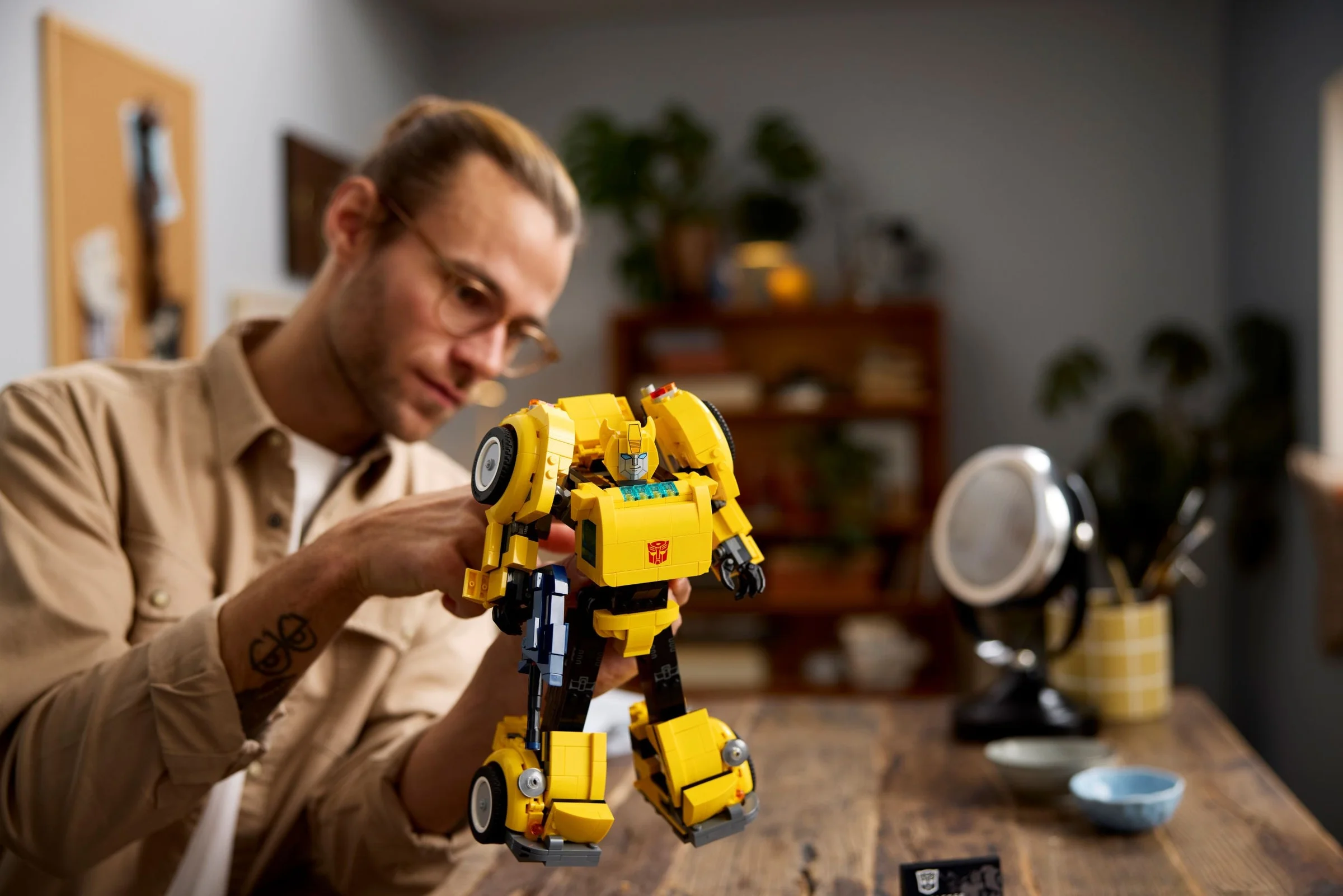 Un adult ține Bumblebee, modelul LEGO 10338, într-o cameră de zi luminoasă.