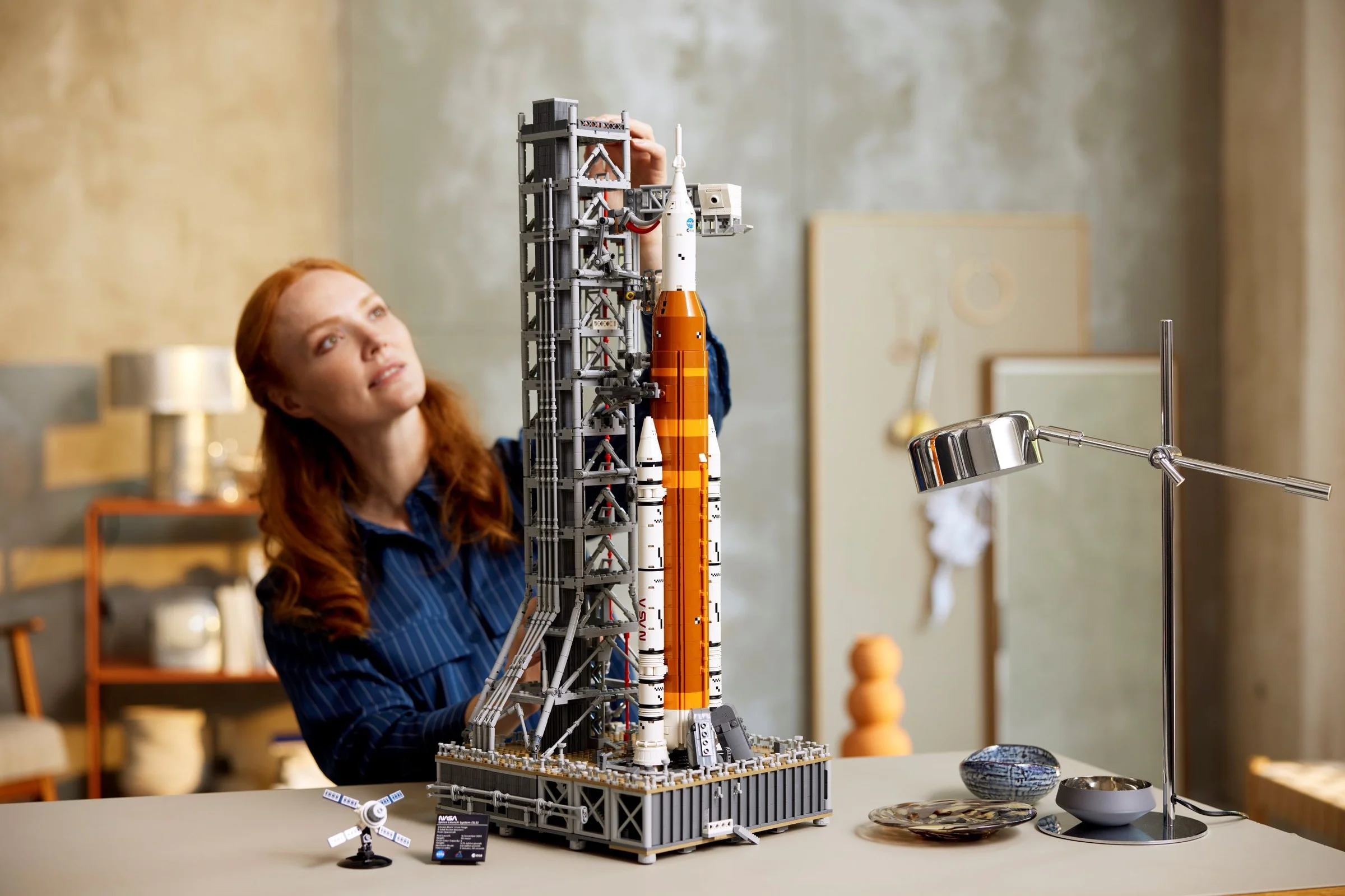 Femeie admirând modelul LEGO NASA Artemis Space Launch System, complex și detaliat.