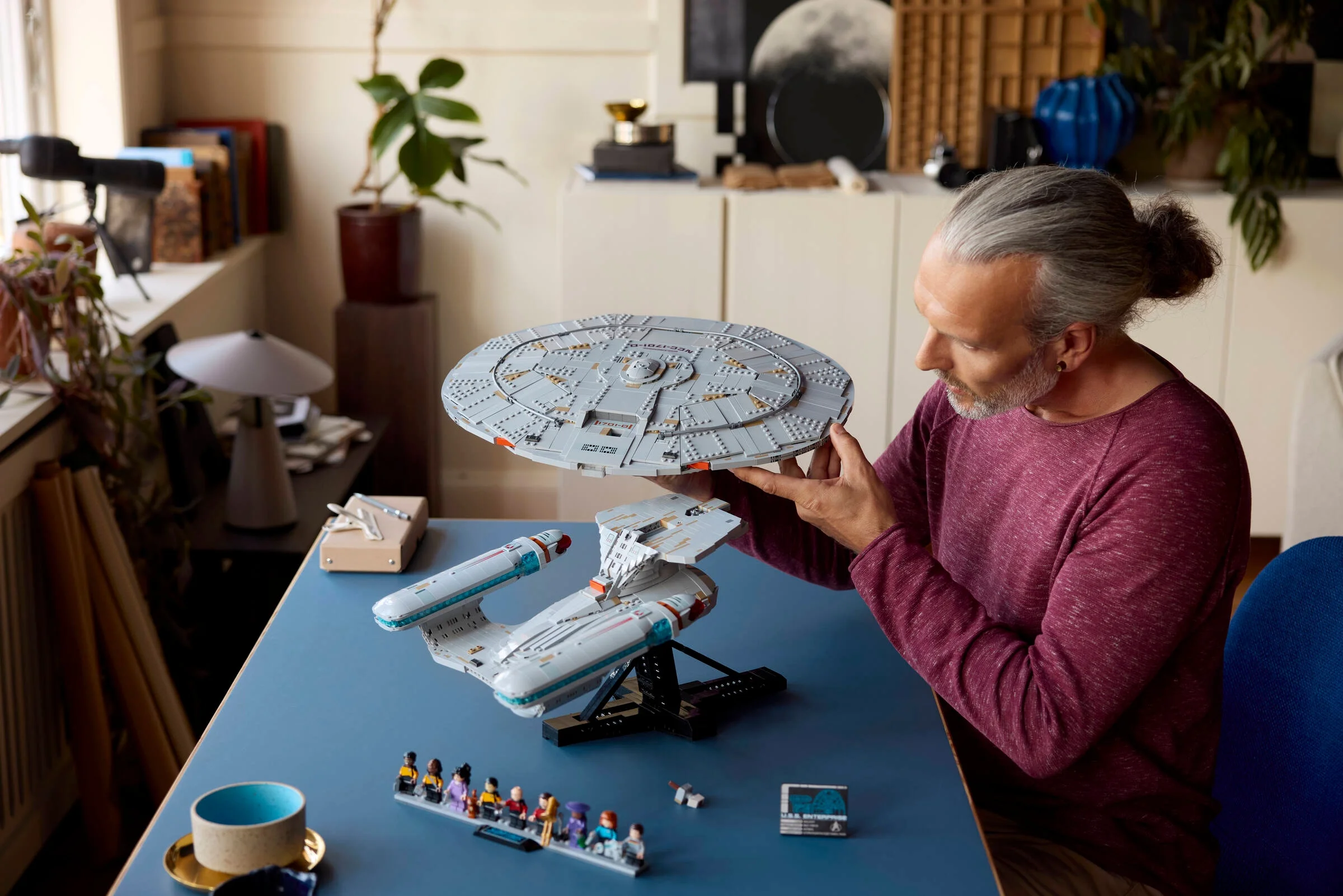 Bărbat admirând modelul LEGO U.S.S. Enterprise NCC-1701-D. Machetă detaliată, minifigurine incluse.