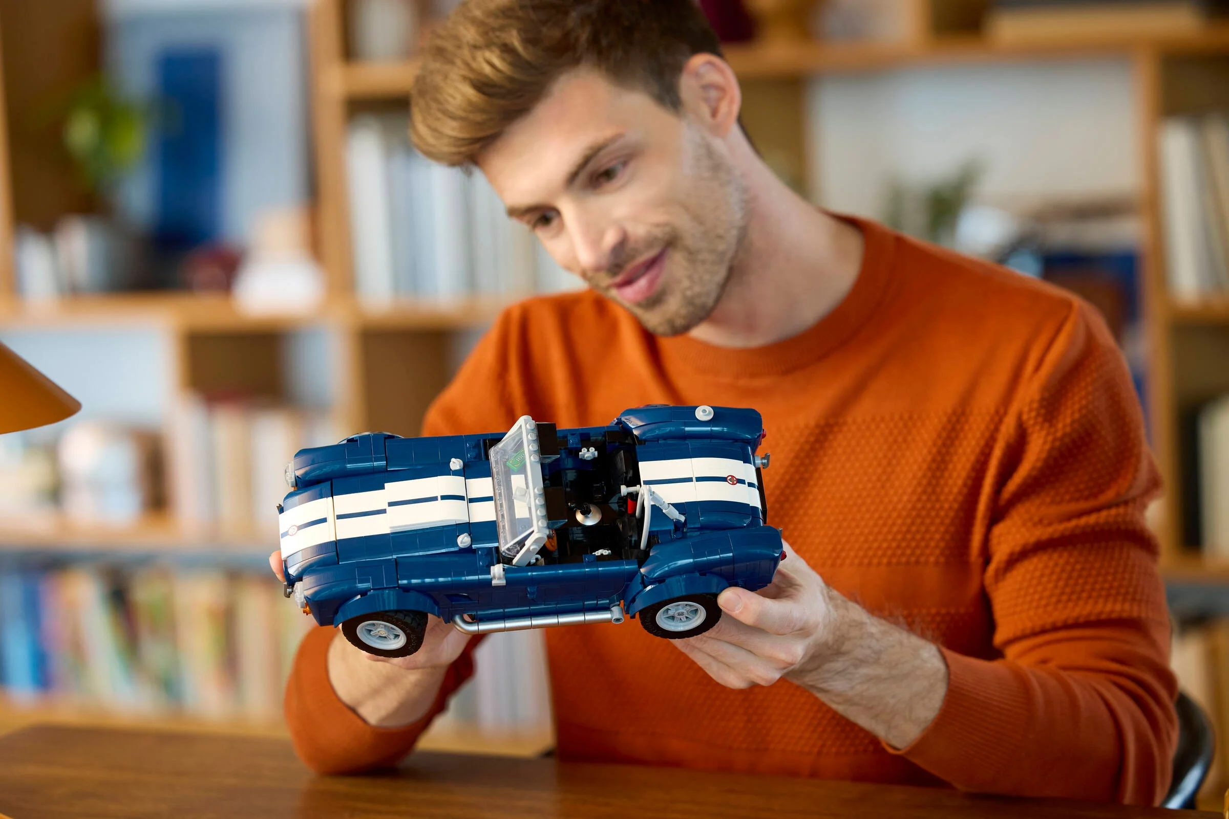 Bărbat admirând modelul LEGO Shelby Cobra 427 S/C, o mașină albastră cu detalii albe.