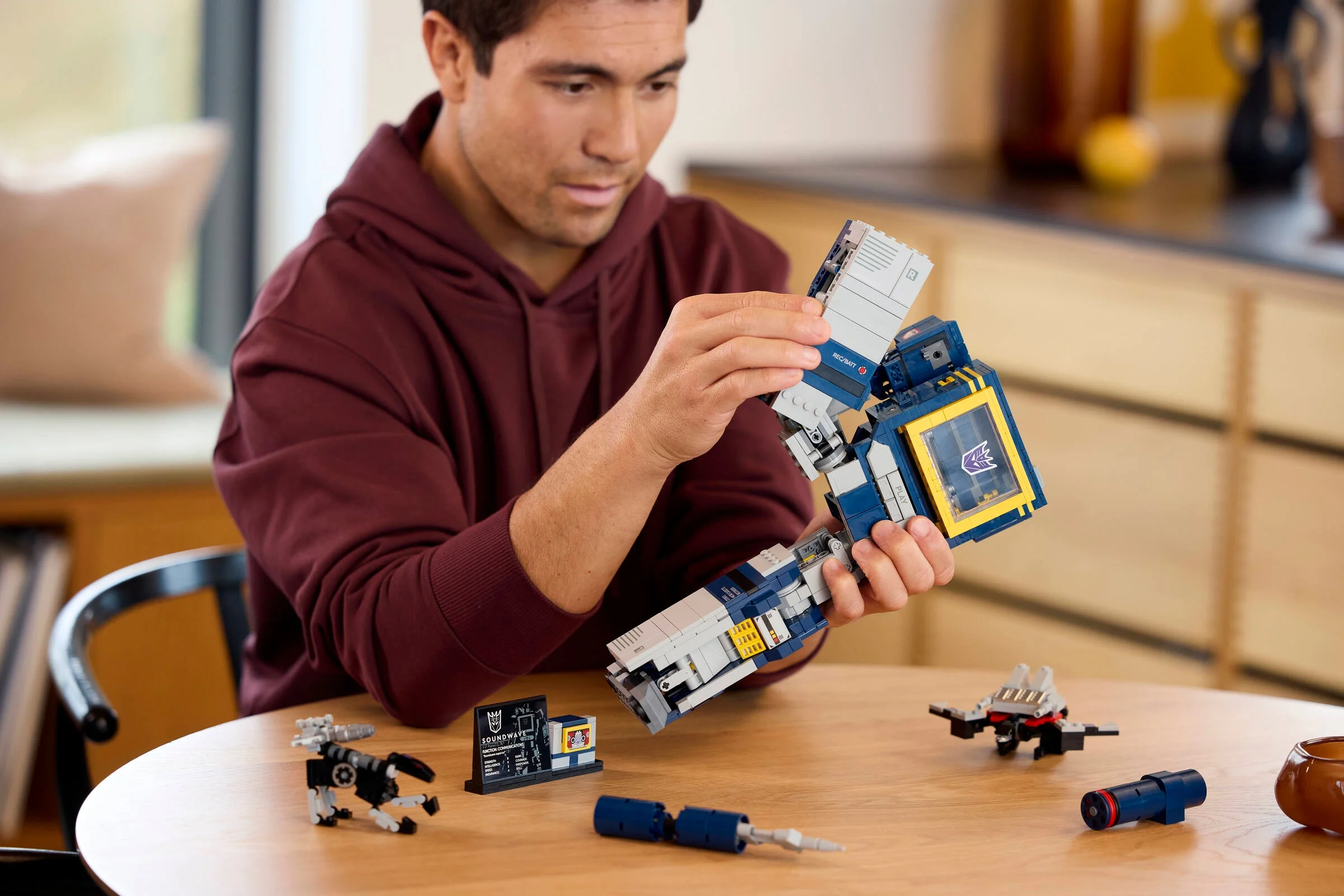 Un adult manevrează Soundwave LEGO, prezentând transformarea. Imagine atractivă și detaliată.