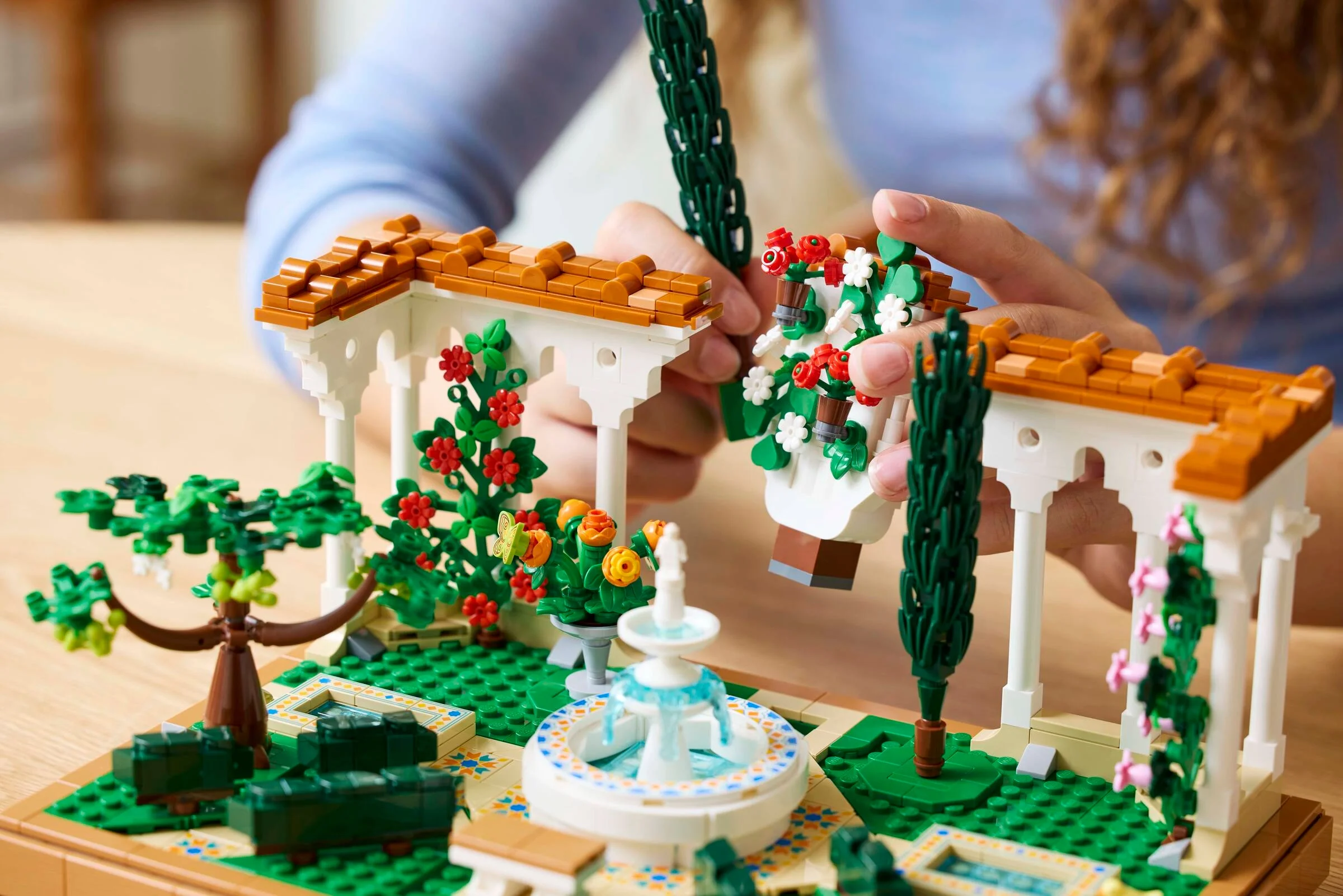 Grădina cu fântână LEGO® Icons 10359 în construcție, detaliată și plină de flori.
