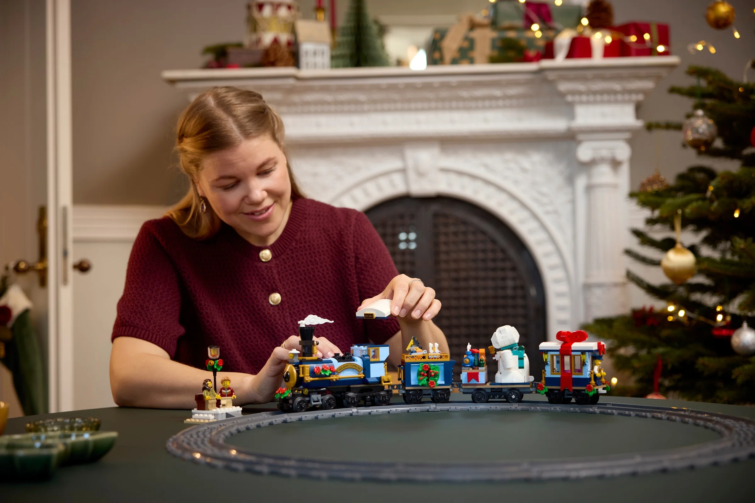Femeie asamblând trenul LEGO Holiday Express 10361. Atmosferă festivă de Crăciun în fundal.