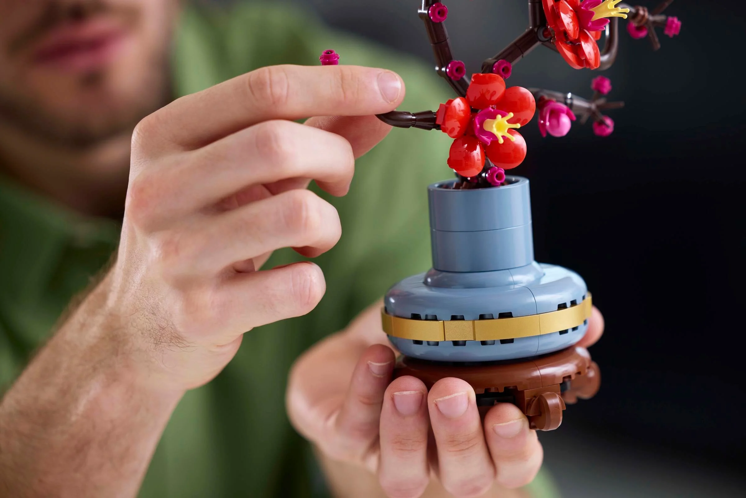 Persoană asamblează un model LEGO cu flori de prun într-un vas albastru.