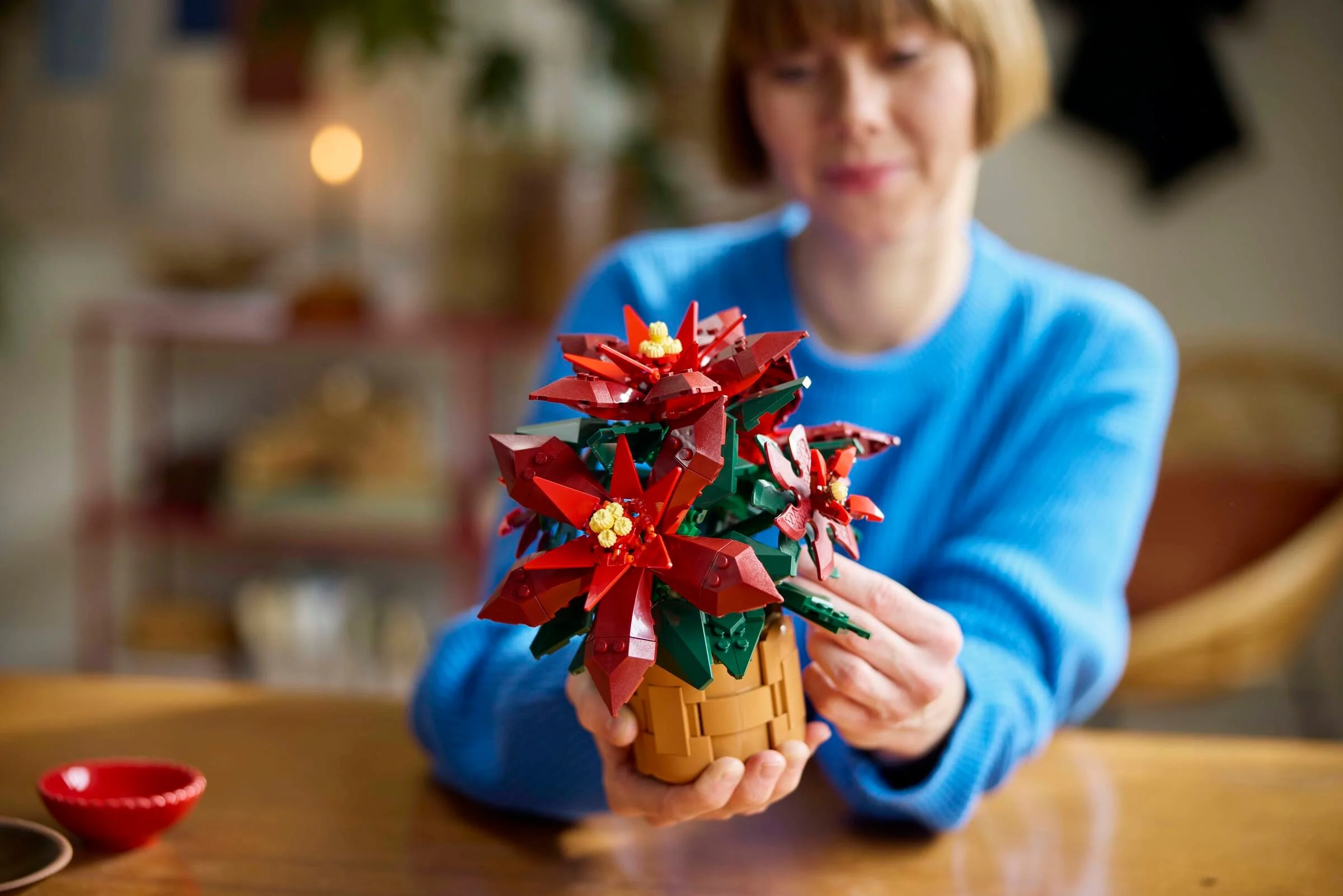 Prim plan cu Poinsettia LEGO 10370 ținută de o persoană, accent pe detalii și aspectul realist.