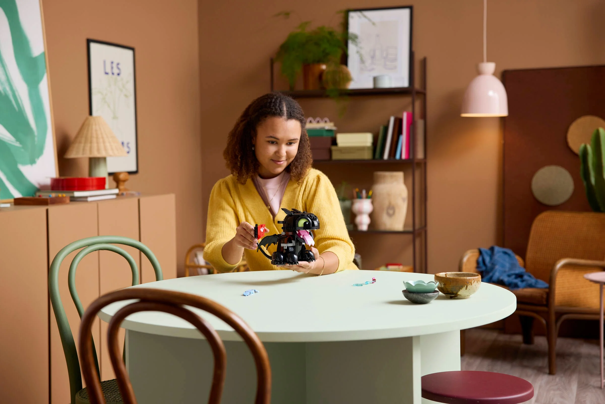 O tânără interacționează cu modelul LEGO Toothless într-o scenă de interior primitoare.