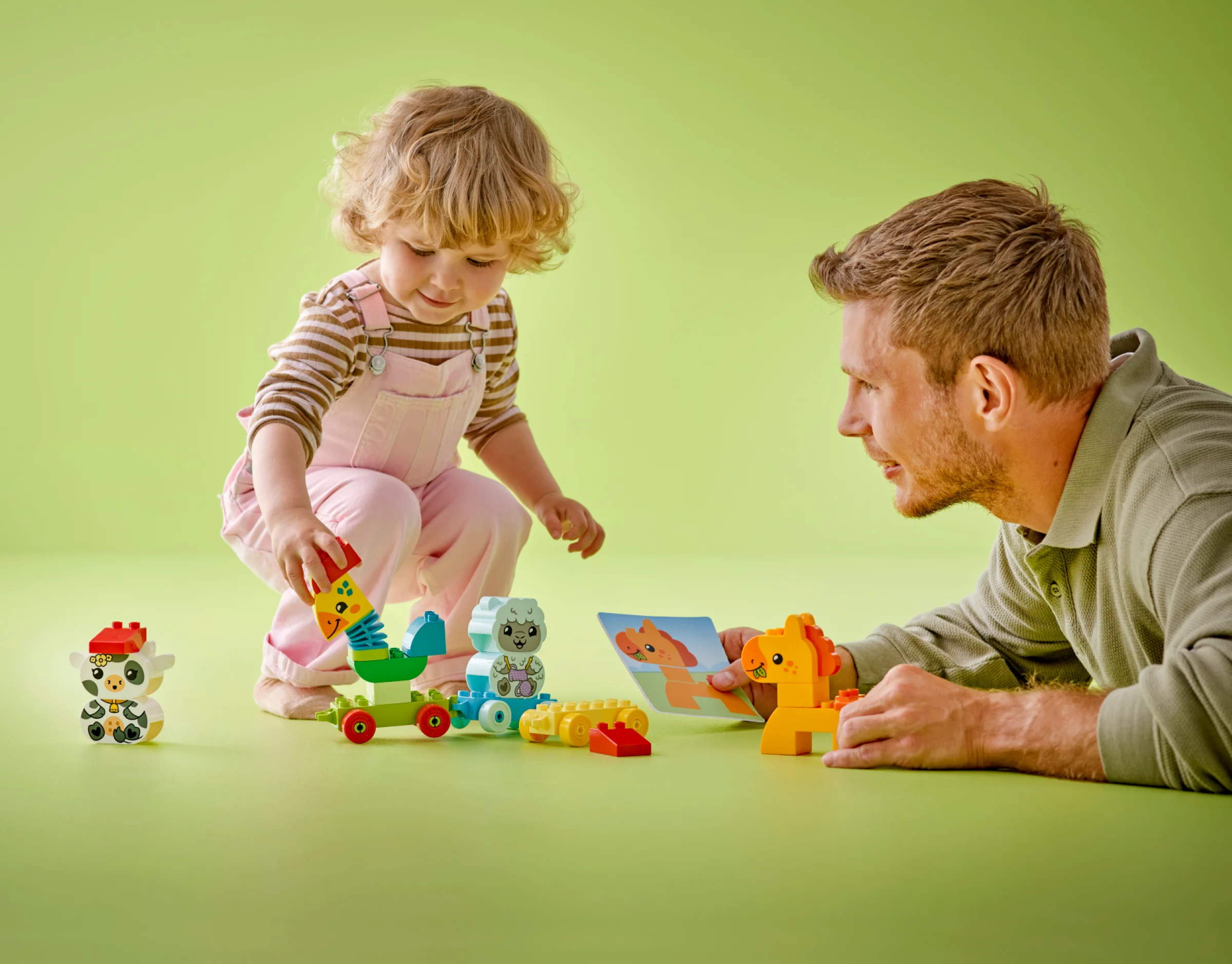 Un copil și un adult se joacă cu trenul LEGO DUPLO cu animale. Set atractiv și educativ.