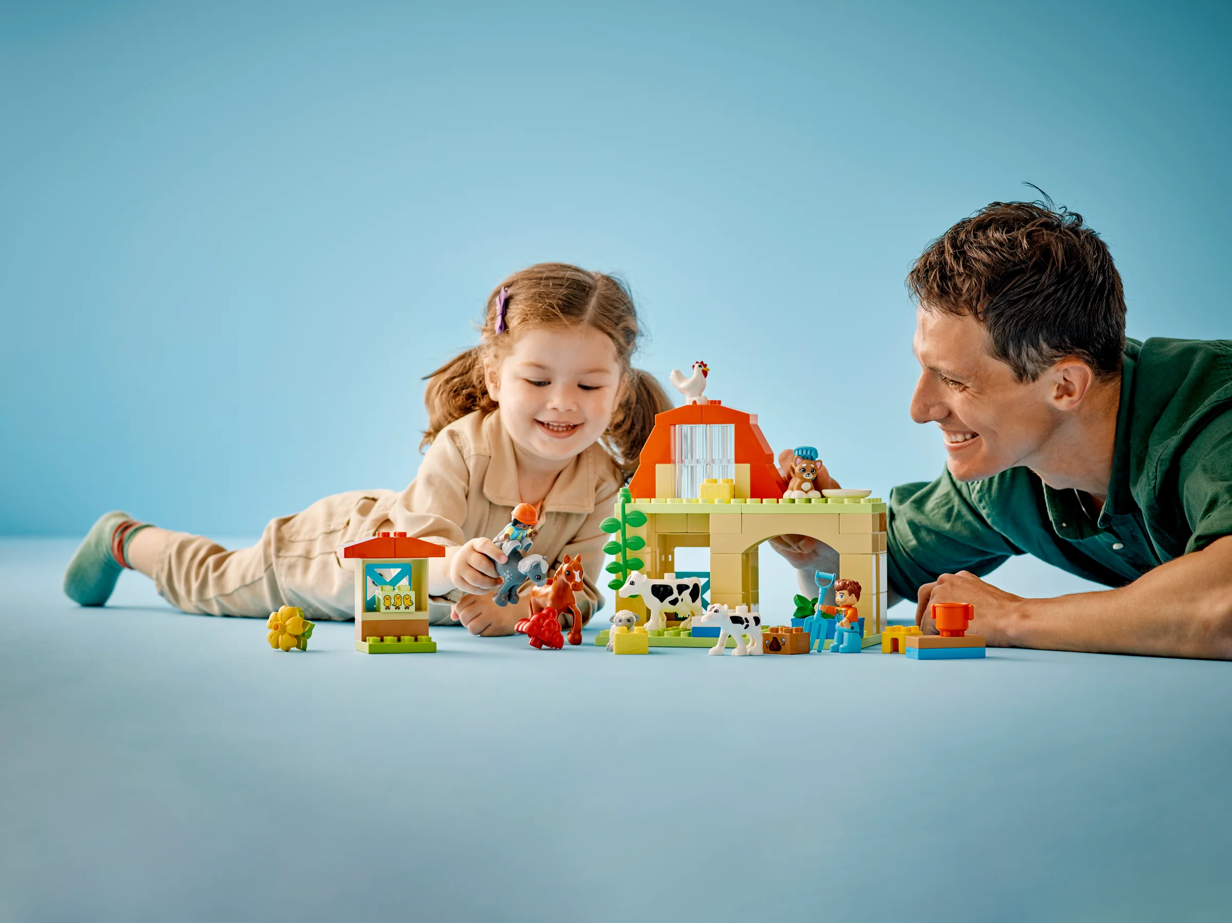 Copil și adult se joacă cu ferma LEGO Duplo, îngrijind animalele. Distracție și învățare timpurie.