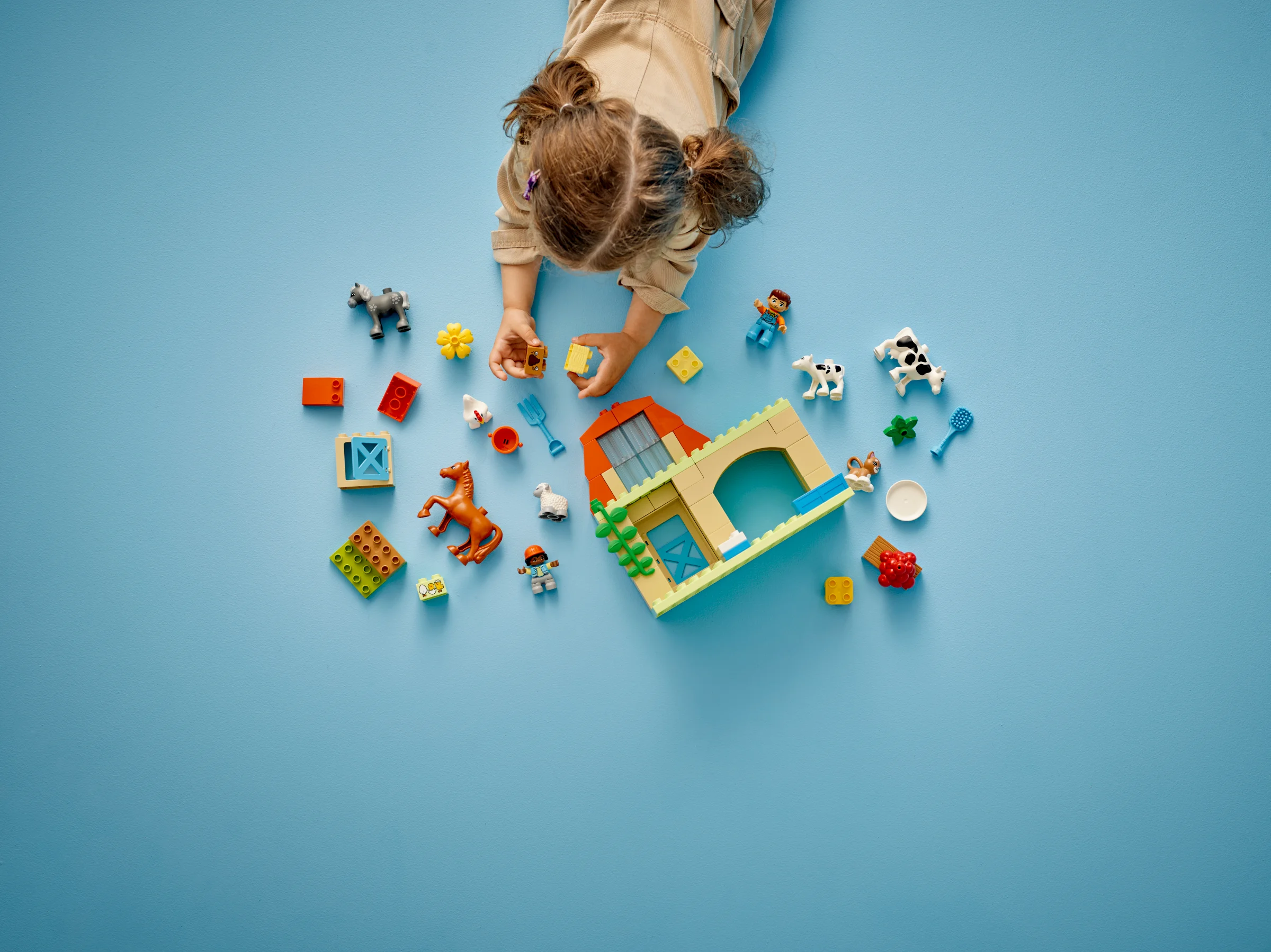 O fetiță se joacă cu setul LEGO Duplo 10416 Fermă. Include animale și o construcție parțial asamblată.
