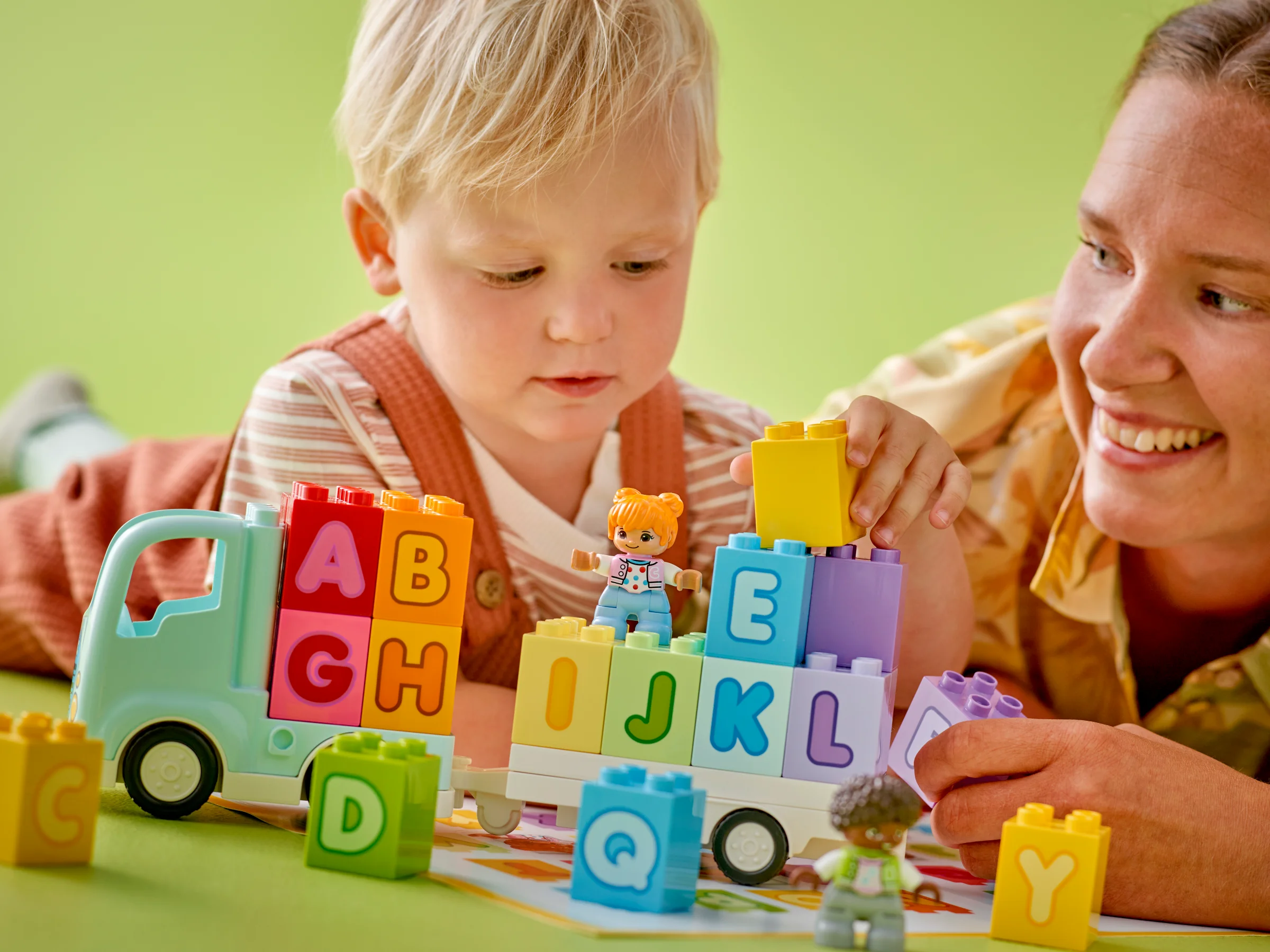 Un copil și o femeie se joacă cu camionul alfabetic Duplo, construind cu blocuri colorate.