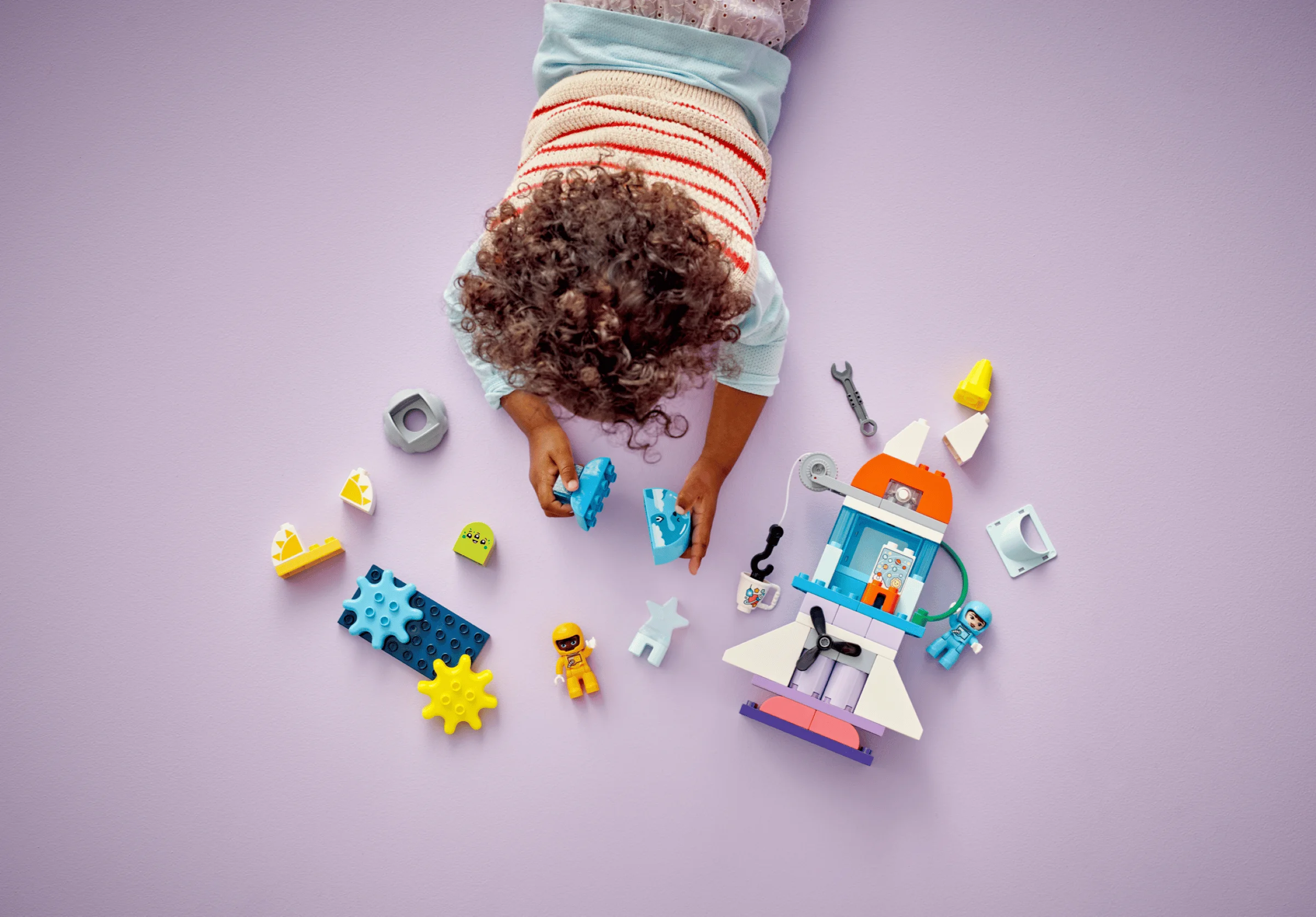 Copil se joacă cu naveta spațială LEGO Duplo, explorând piese și minifigurine colorate.