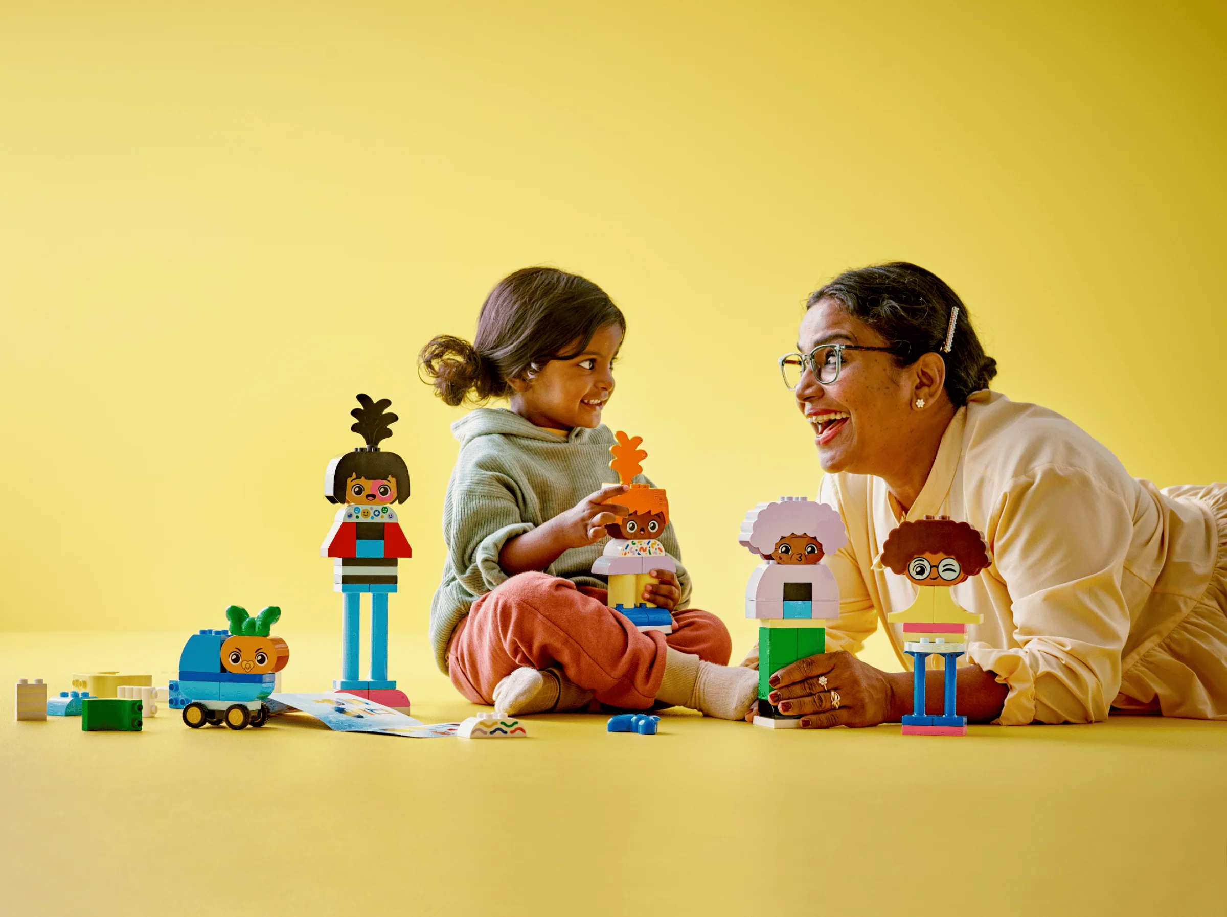 O fetiță și o bunică se joacă împreună cu figurine Duplo, explorând emoțiile și creativitatea.