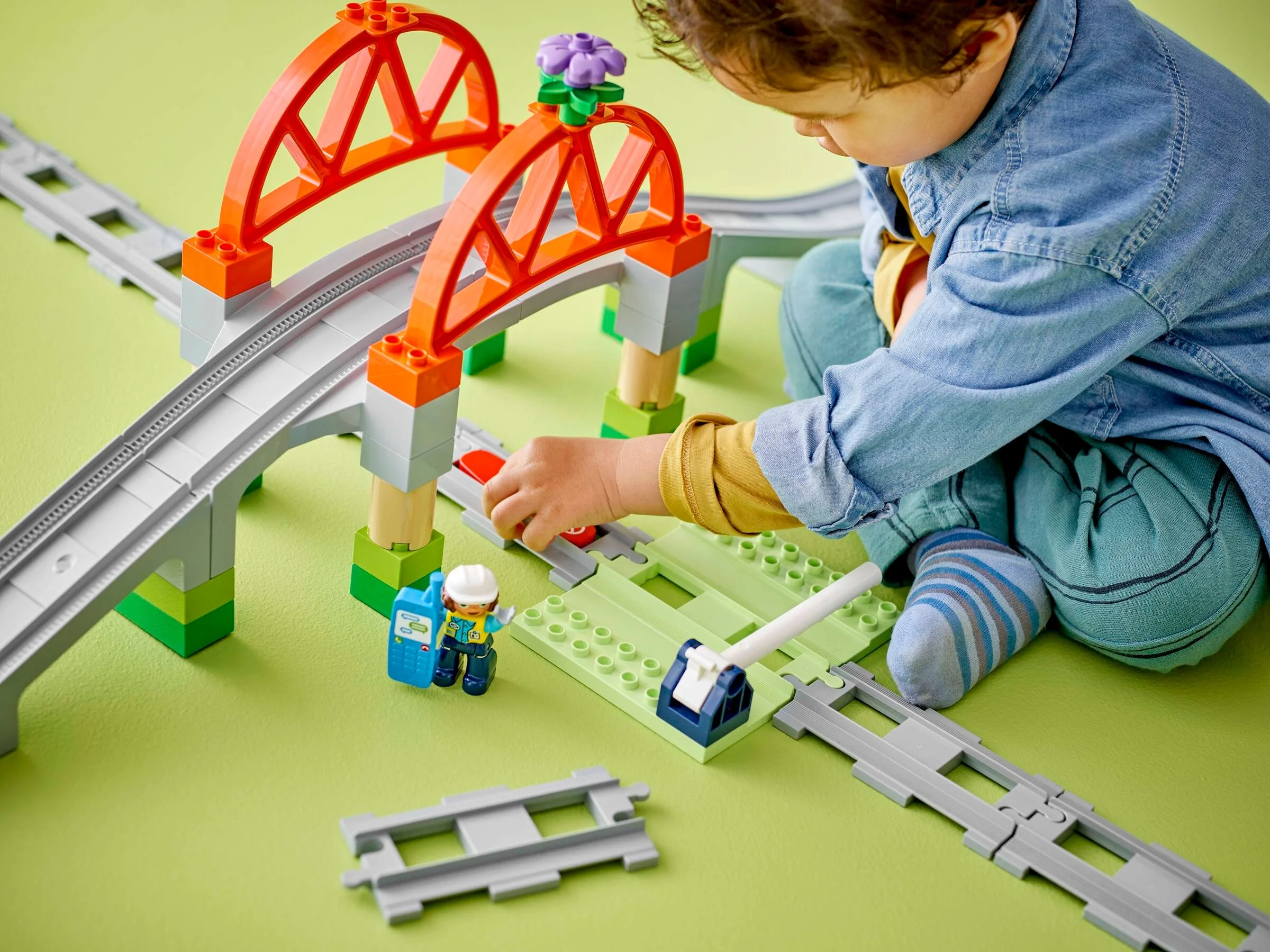 Copil se joacă cu podul și șinele de tren Duplo 10426, explorând setul cu entuziasm.
