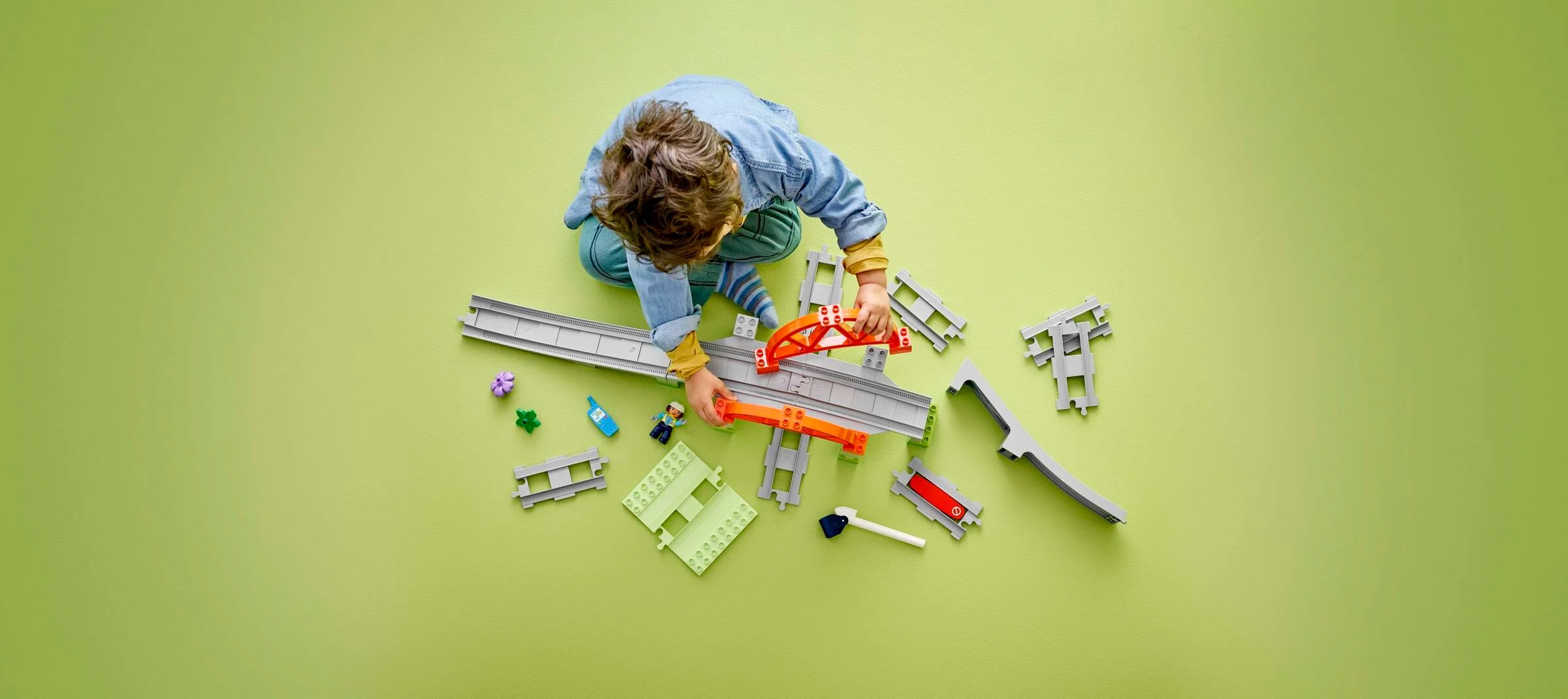 Copil se joacă cu setul LEGO Duplo Tren și Pod cu șine. Imagine de sus.