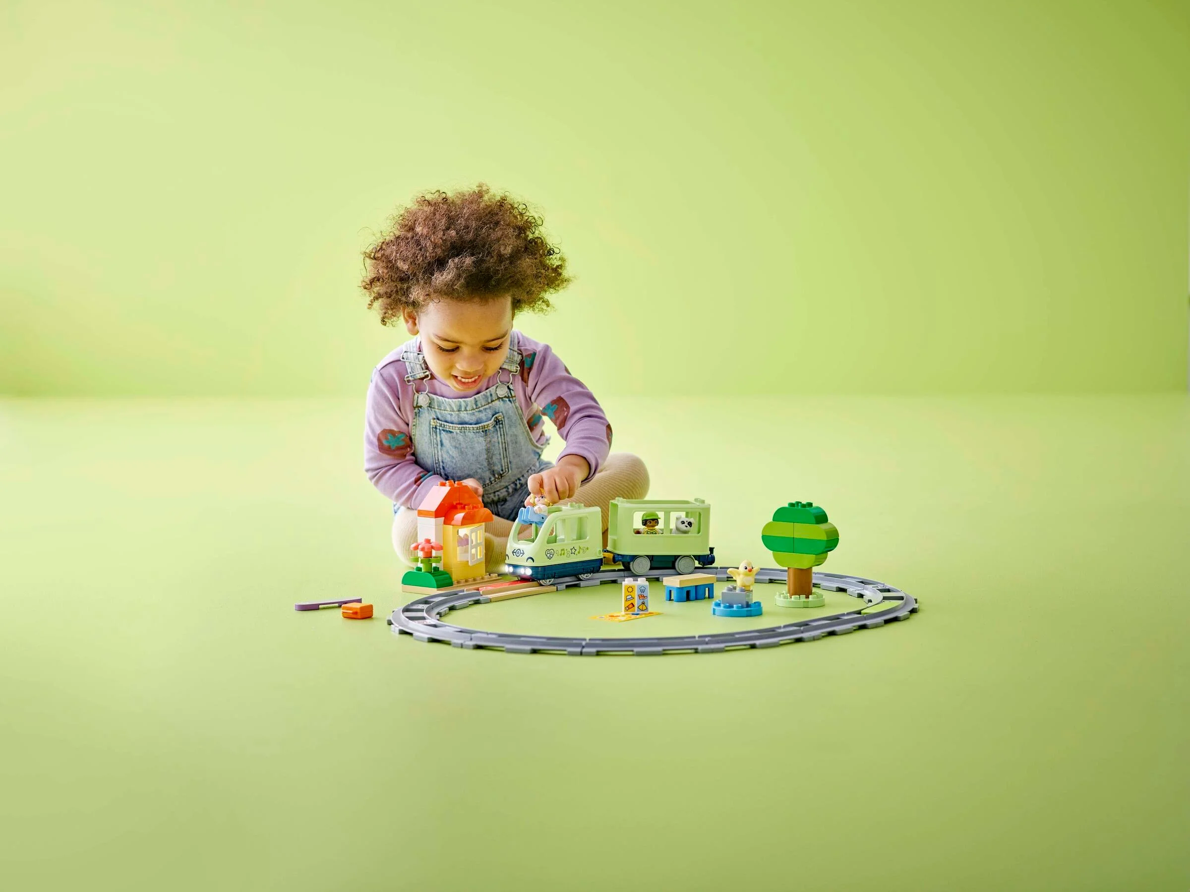 Copil se joacă cu trenul interactiv Duplo pe șine. Casă, copac, figurine incluse.