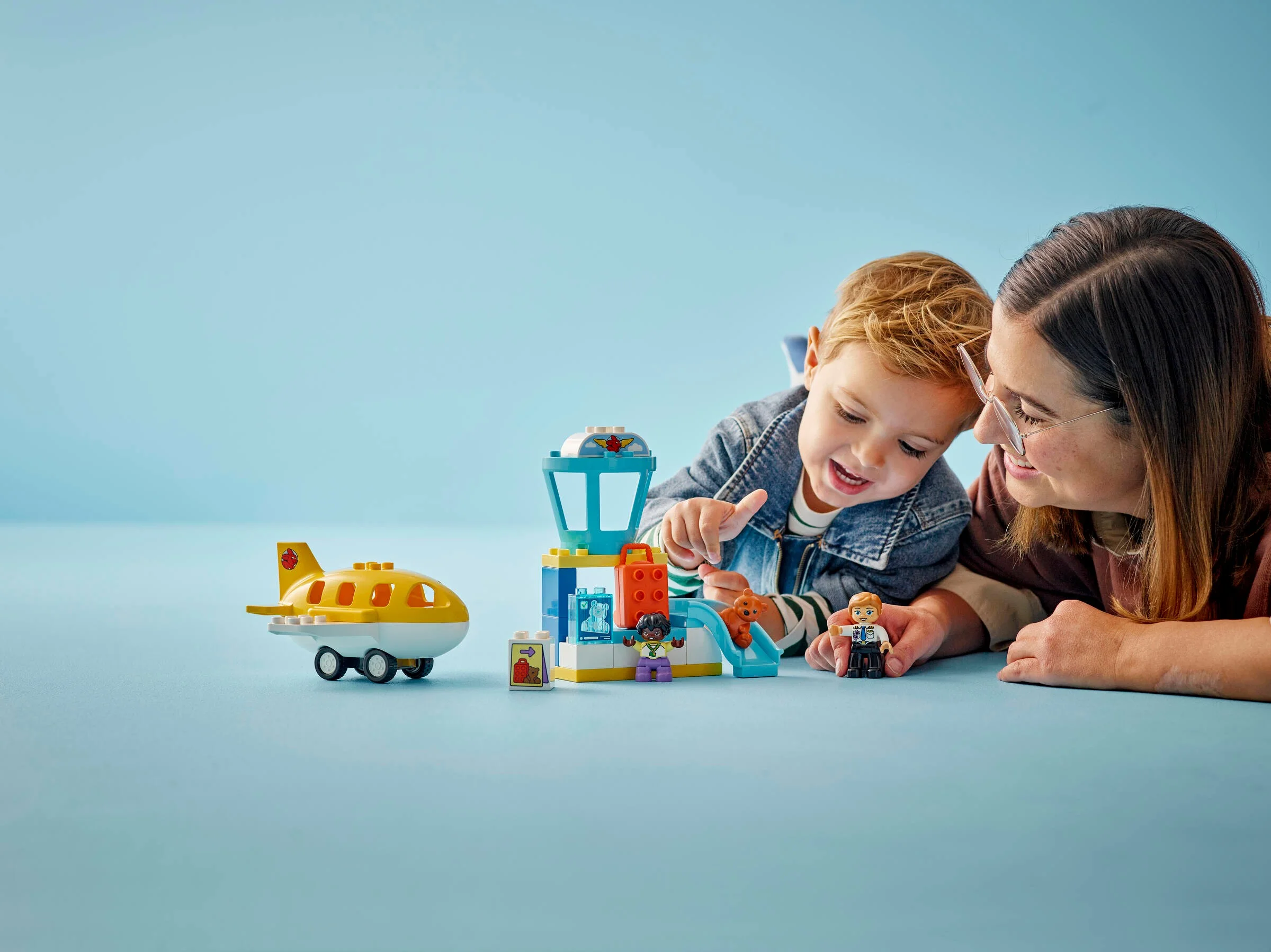 Imagine cu un copil și o femeie jucându-se cu setul LEGO Duplo aeroport. Atmosferă prietenoasă.