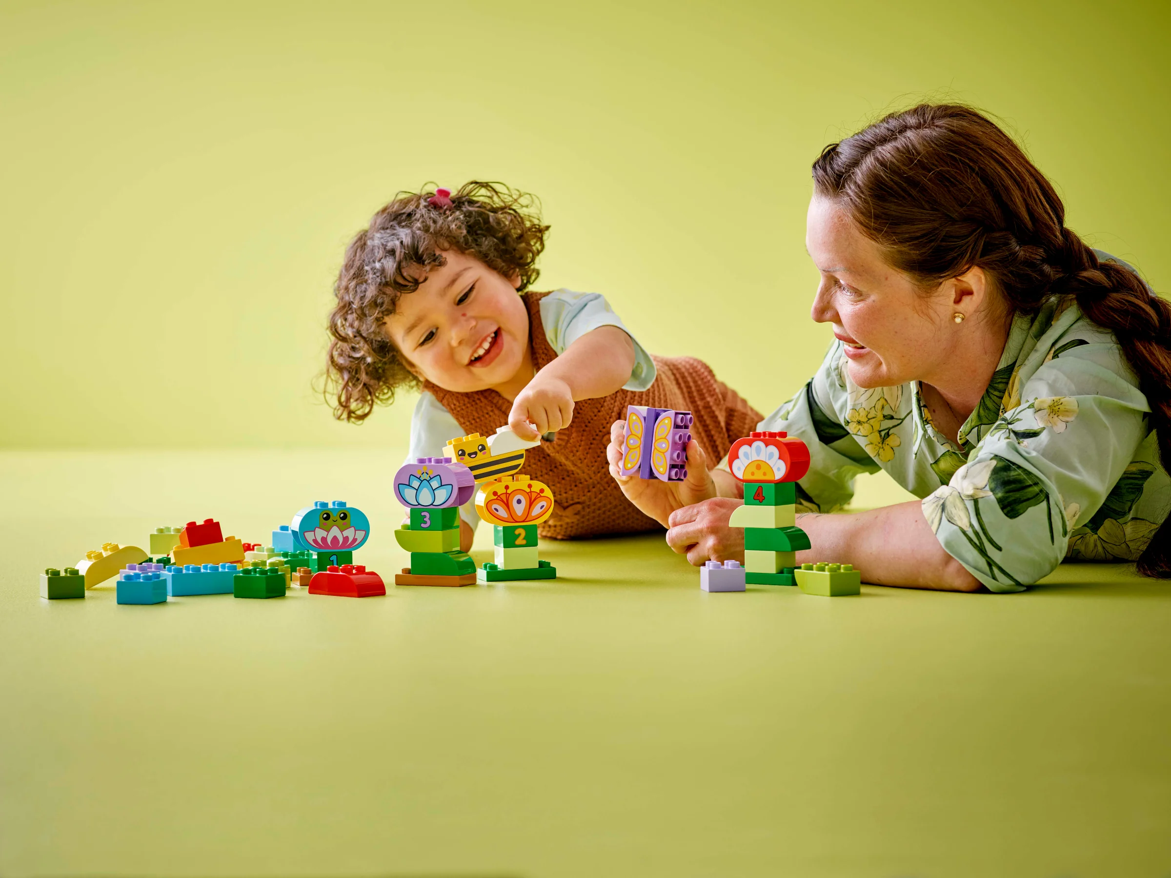 Copil și adult construind flori colorate Duplo. Joacă creativă și distracție împreună.