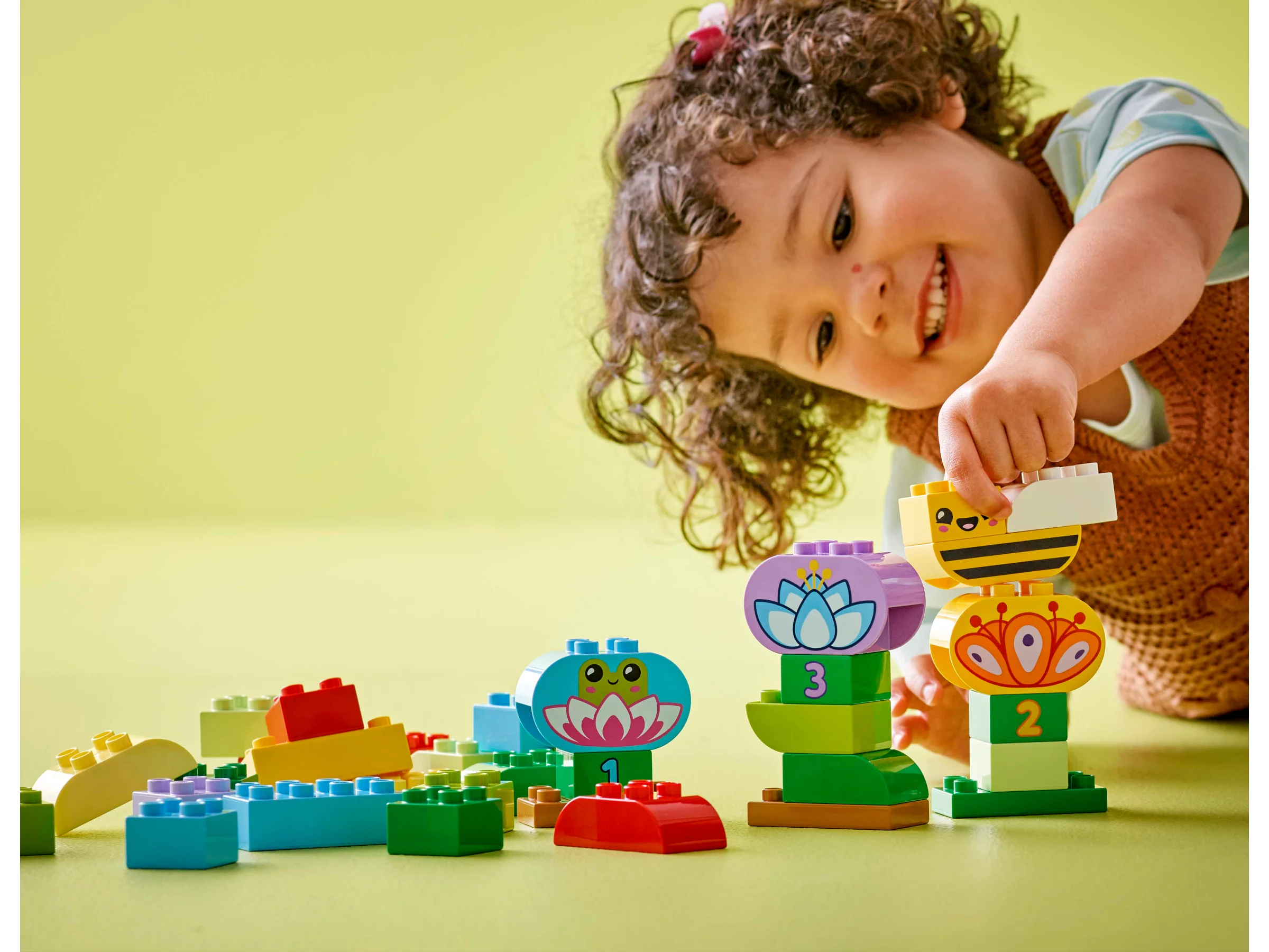Fetiță zâmbitoare se joacă cu florile și insectele LEGO® DUPLO®. Distracție creativă garantată!