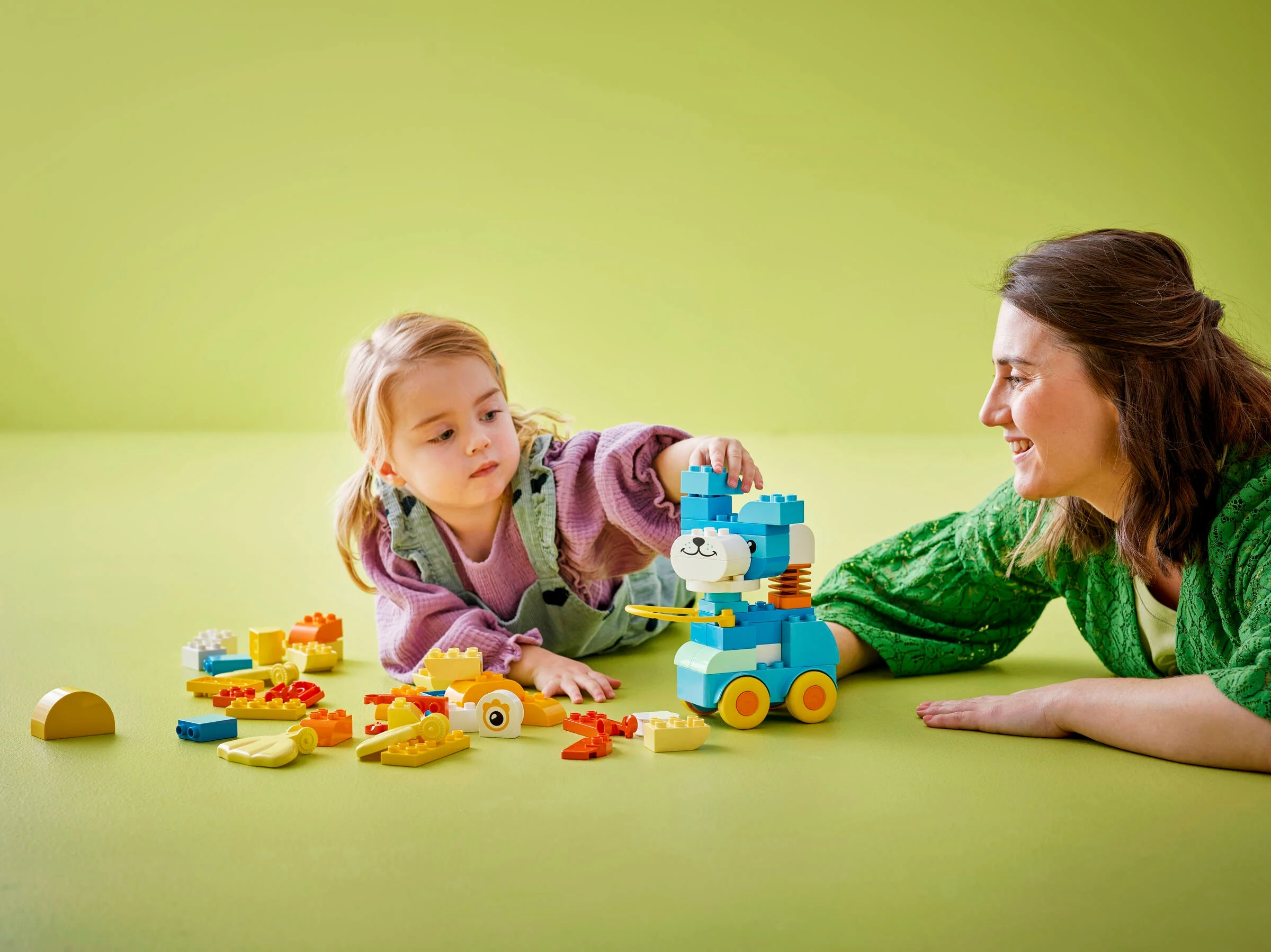Fetiță și femeie construind un animal pe roți Duplo albastru. Distracție cu jucării, zâmbete și creativitate.