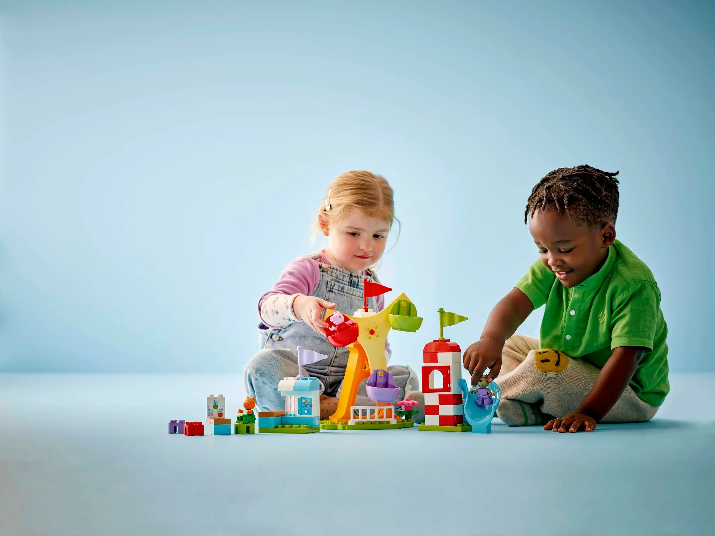 Doi copii se joacă cu setul LEGO Duplo 10453, construind un bâlci distractiv. Scene luminoase și pline de culoare.