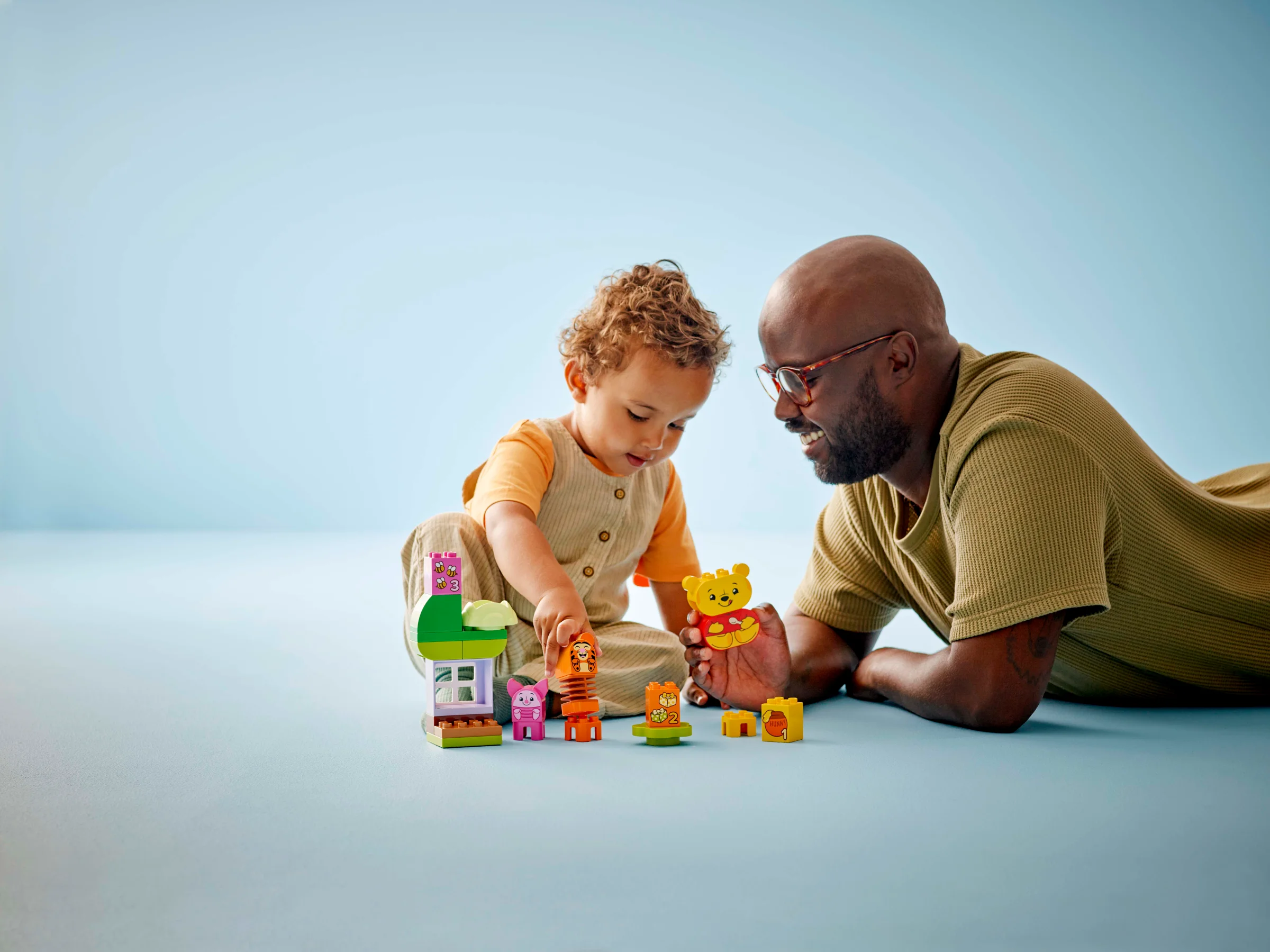 Copil și adult jucând cu setul LEGO Duplo Winnie the Pooh. Construcție colorată, atmosferă caldă.