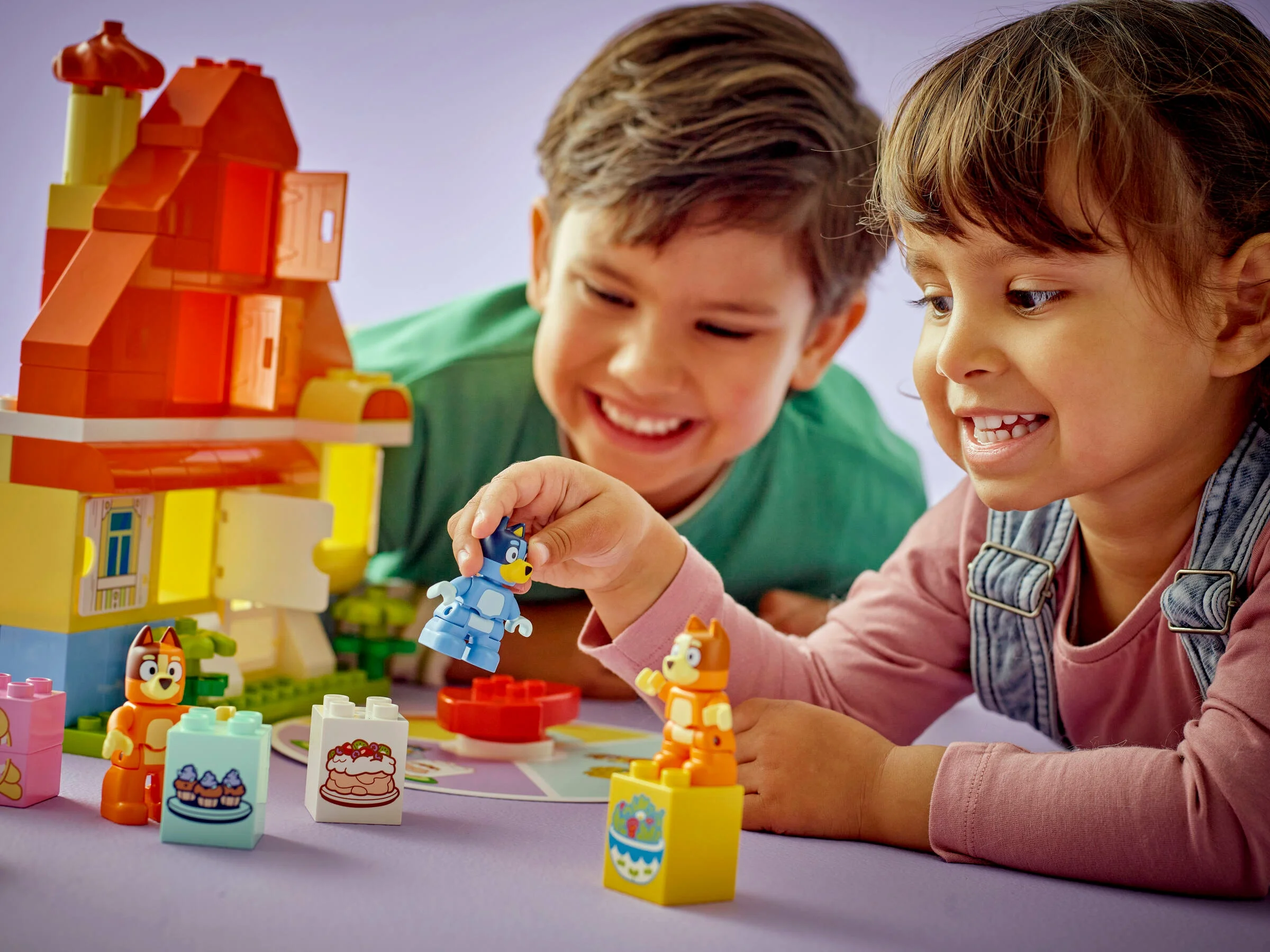 Copii zâmbitori se joacă cu Bluey's Family House și cu jocul de memorie Duplo.