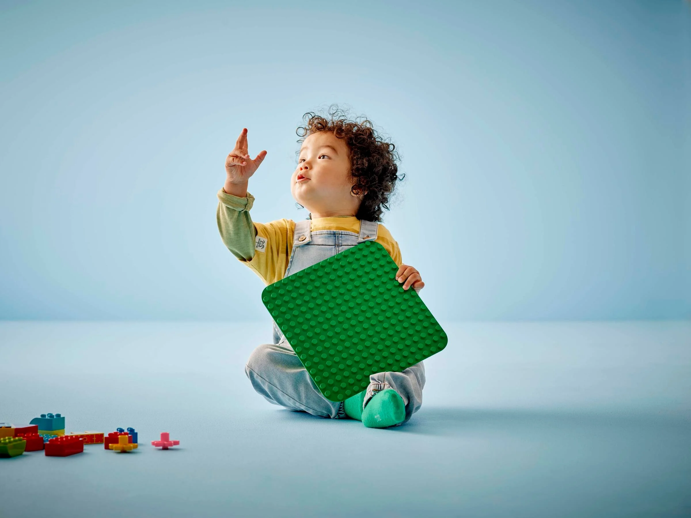 Copil ține o placă verde Duplo, explorând creativ cu LEGO. Distracție și joacă!