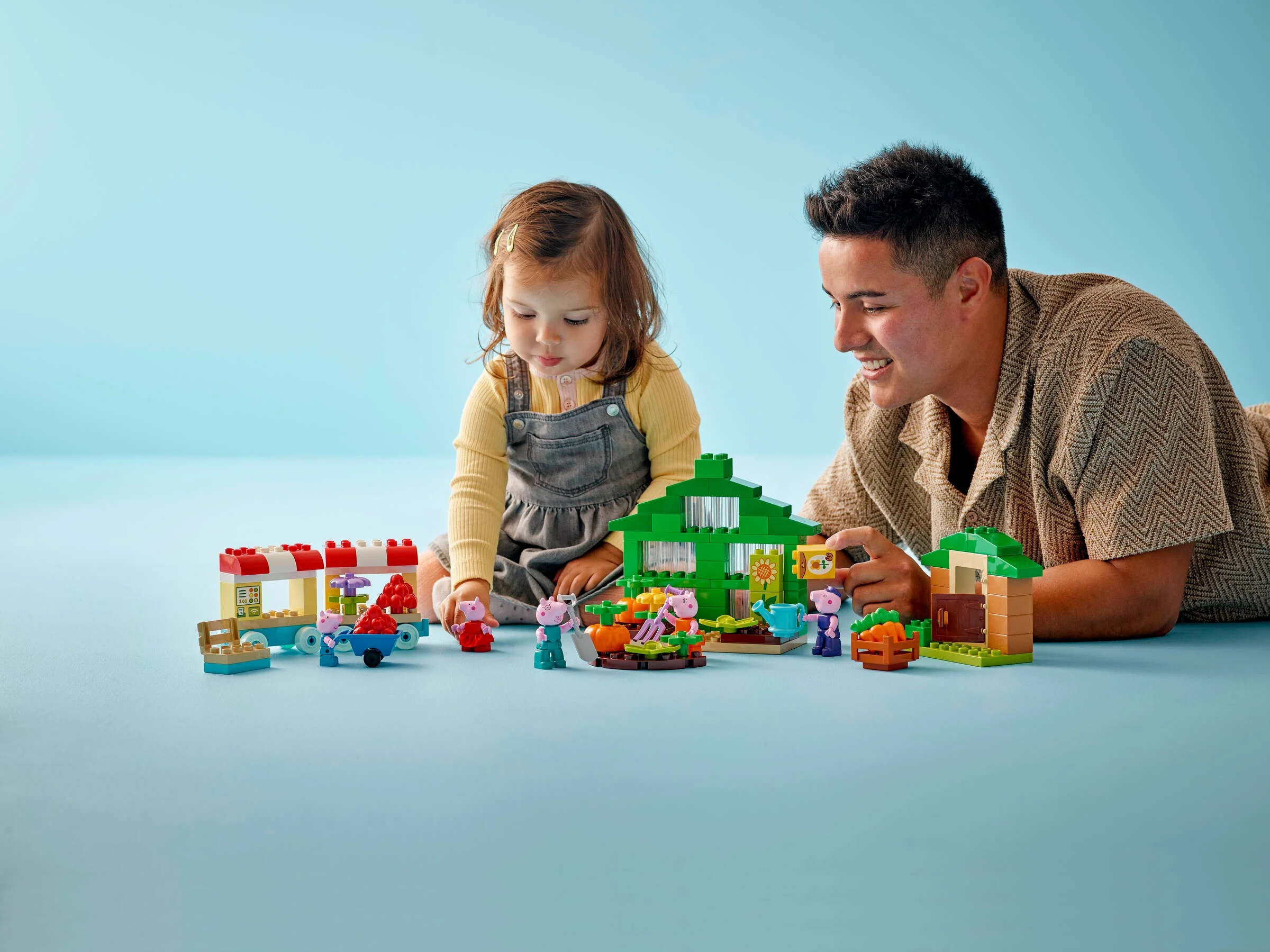 O fetiță și un adult se joacă cu setul LEGO Duplo Grădina și Sera lui Bunicul Porc.