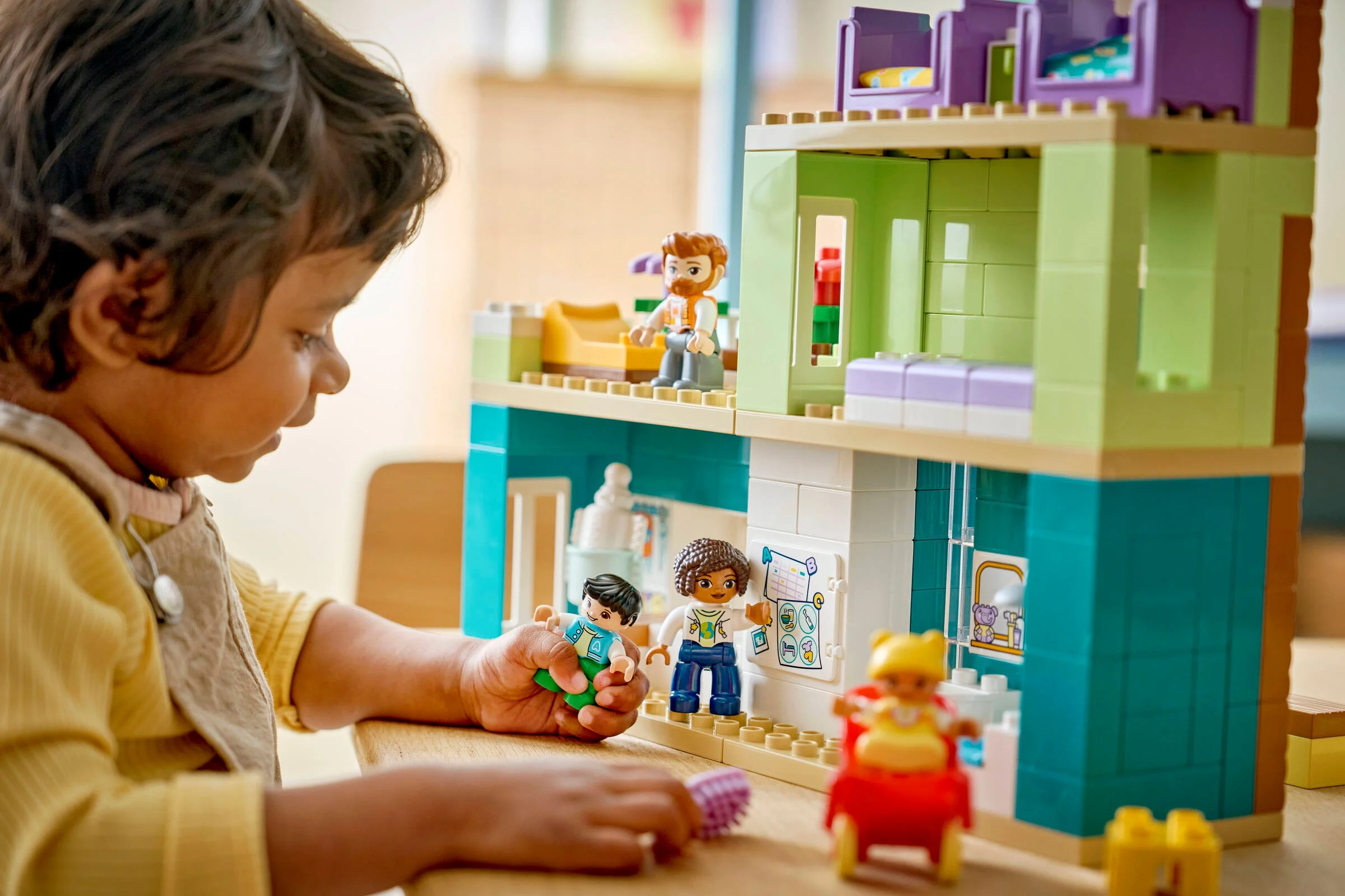 Copil se joacă cu casa Duplo, cu minifigurinele incluse, într-o imagine luminoasă și colorată.