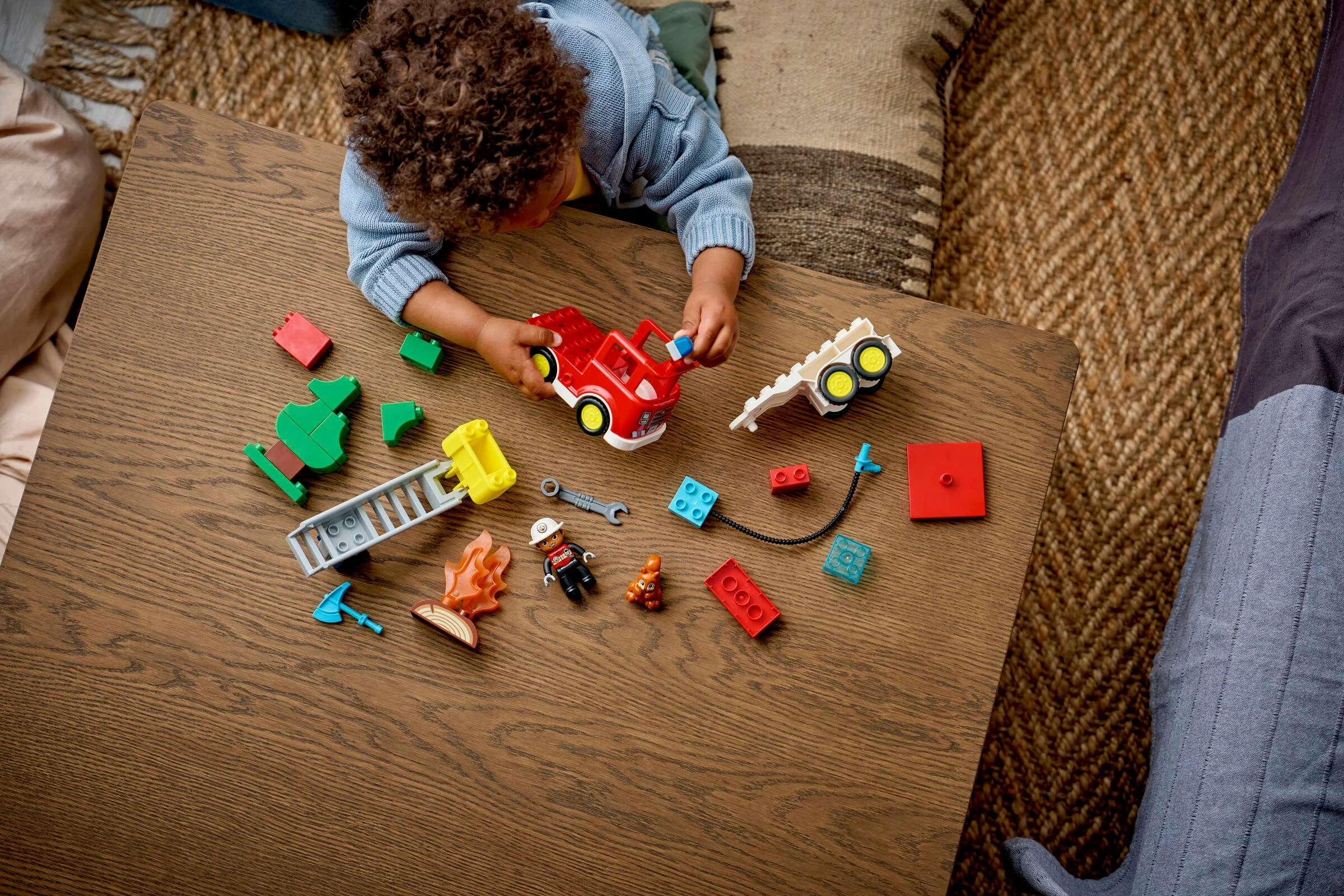 Un copil se joacă cu camionul de pompieri și alte piese LEGO Duplo, explorând creativitatea.