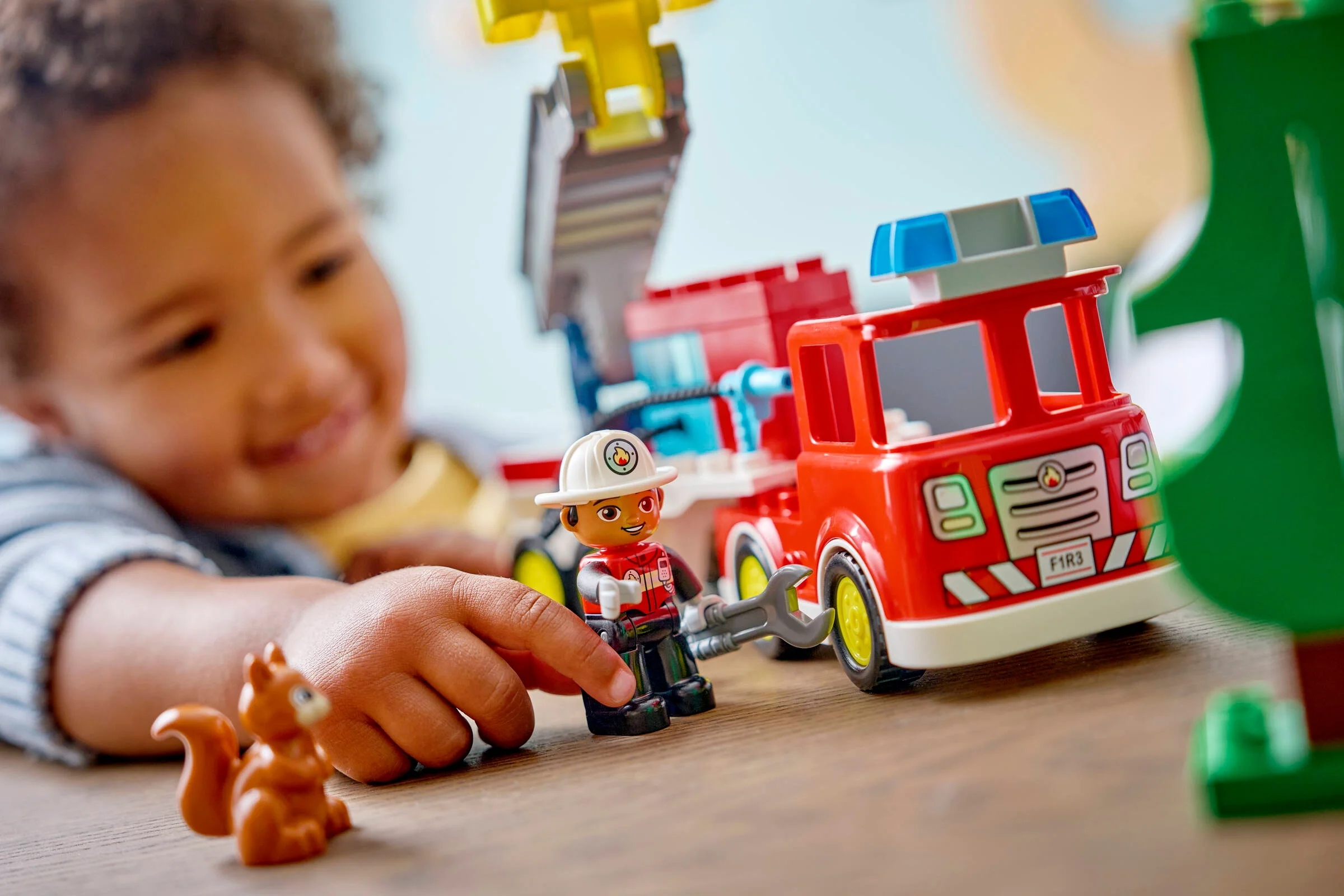 Un copil se joacă cu camionul de pompieri Duplo, minifigurina pompier și o veveriță.