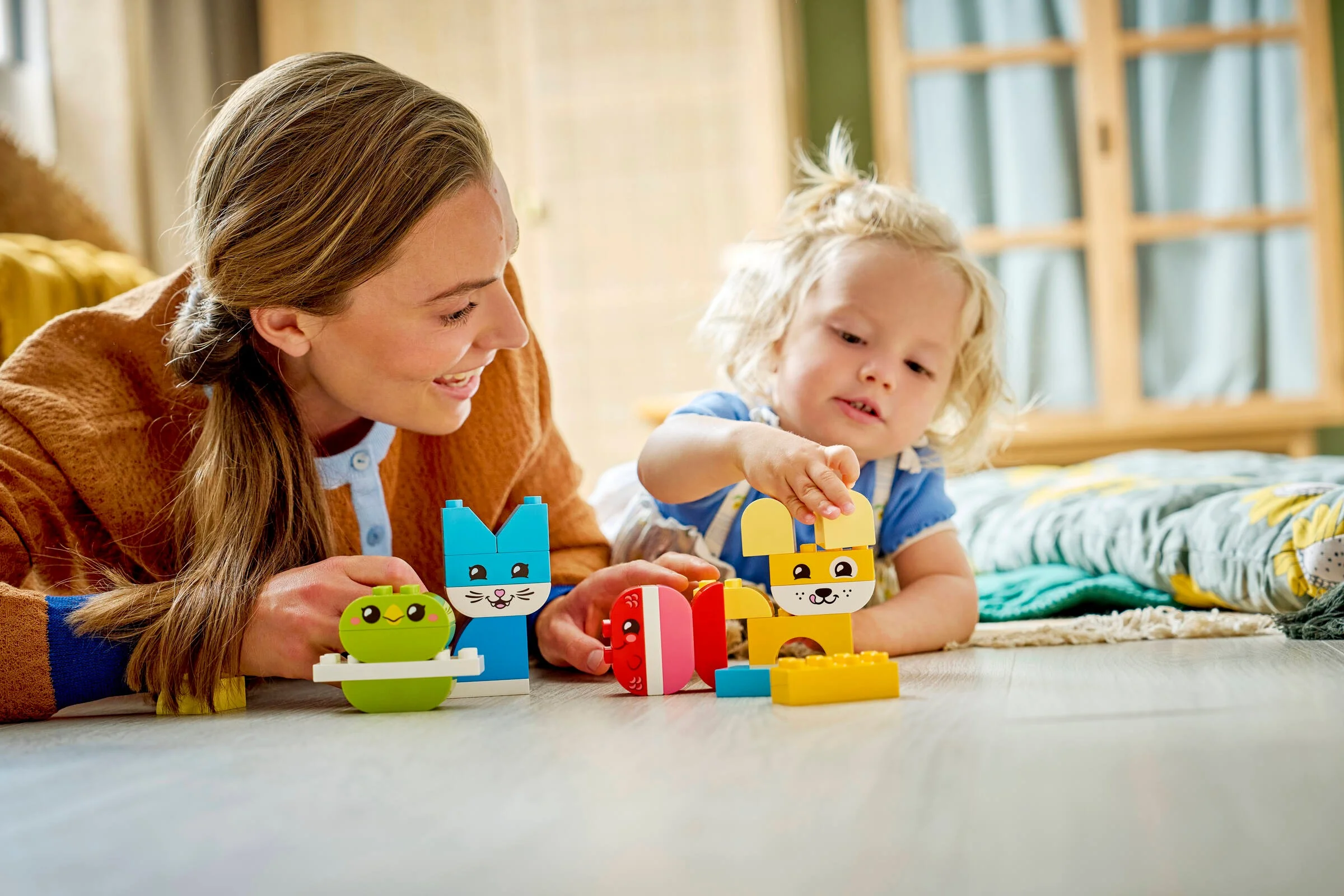 Mamă și copil construind animale drăguțe din cărămizi LEGO Duplo colorate.