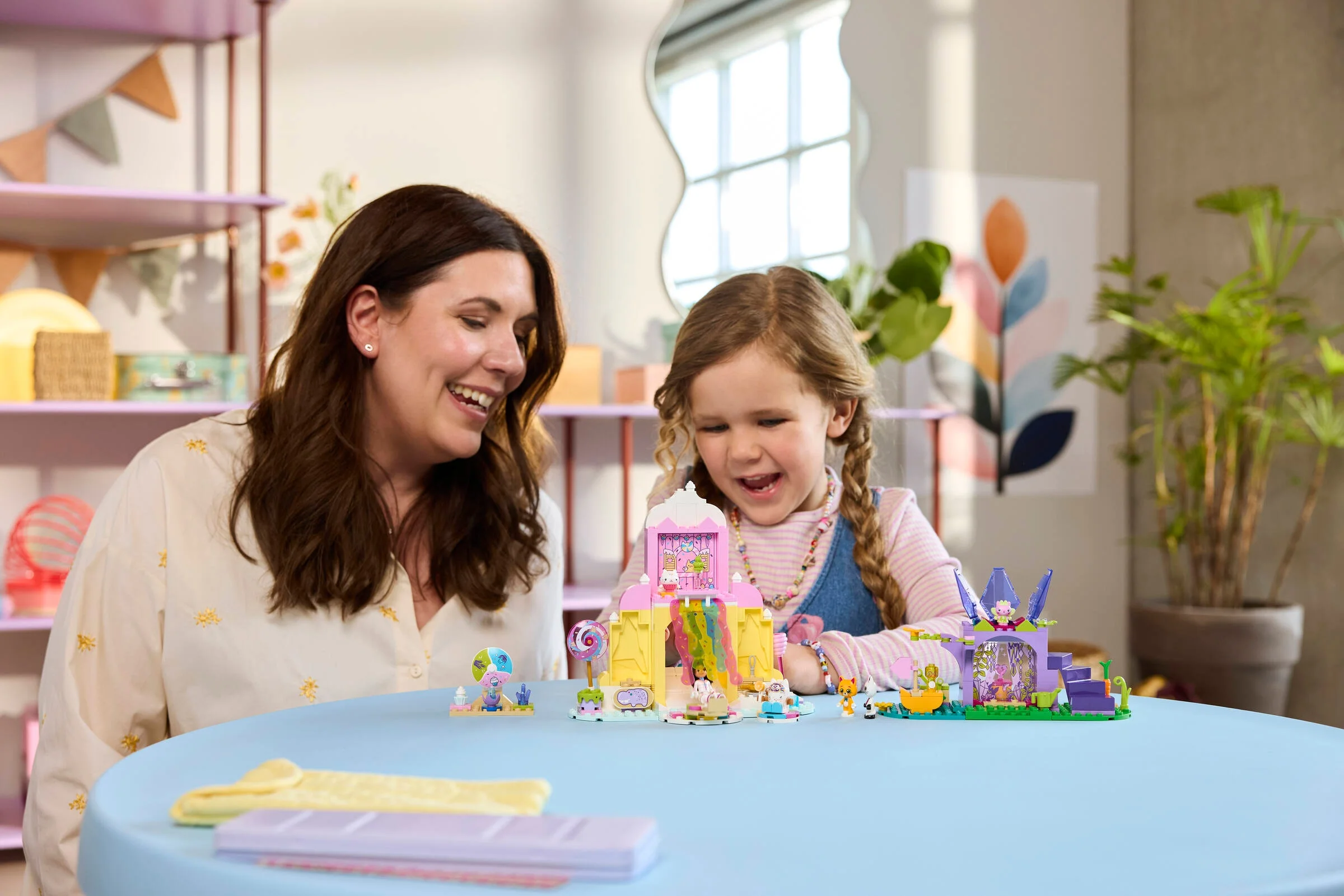 O mamă și fiica se joacă cu setul LEGO Gabby's Dollhouse, zâmbind.