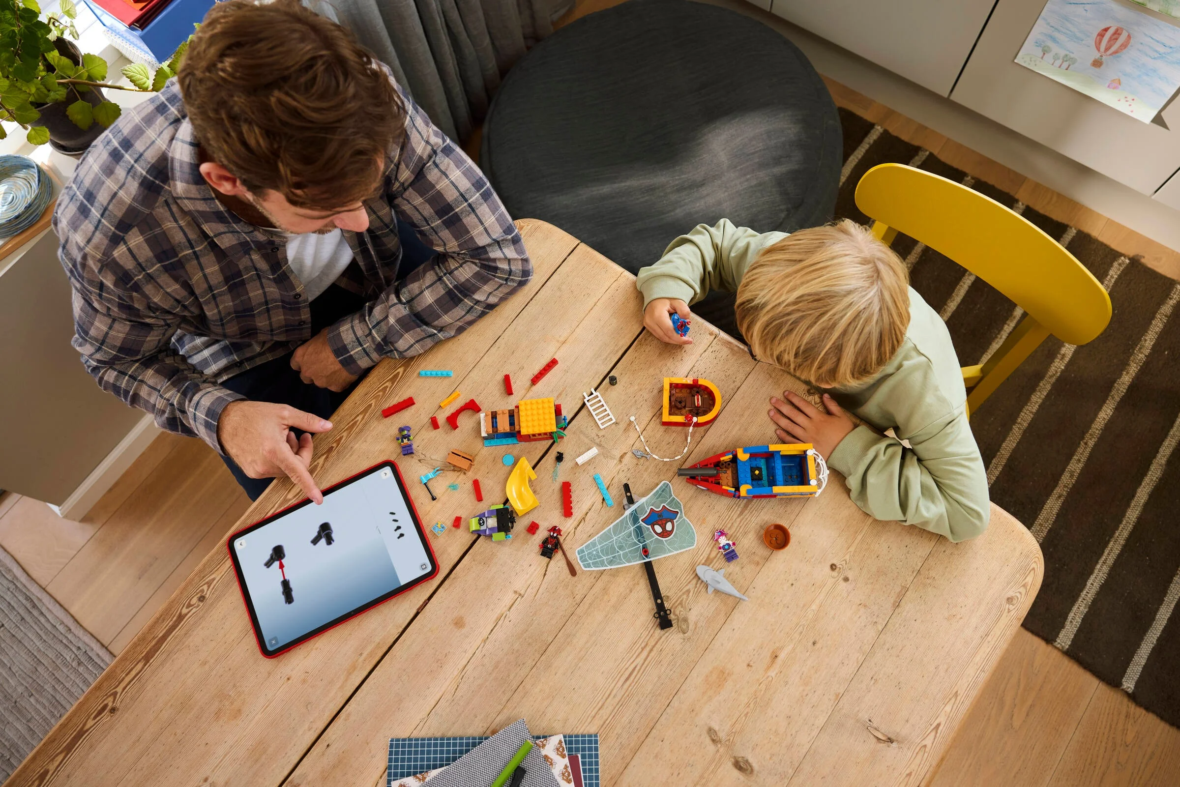 Copil și adult construind împreună setul LEGO 11208 „Corabia Piraților Team Spidey”, folosind o tabletă.