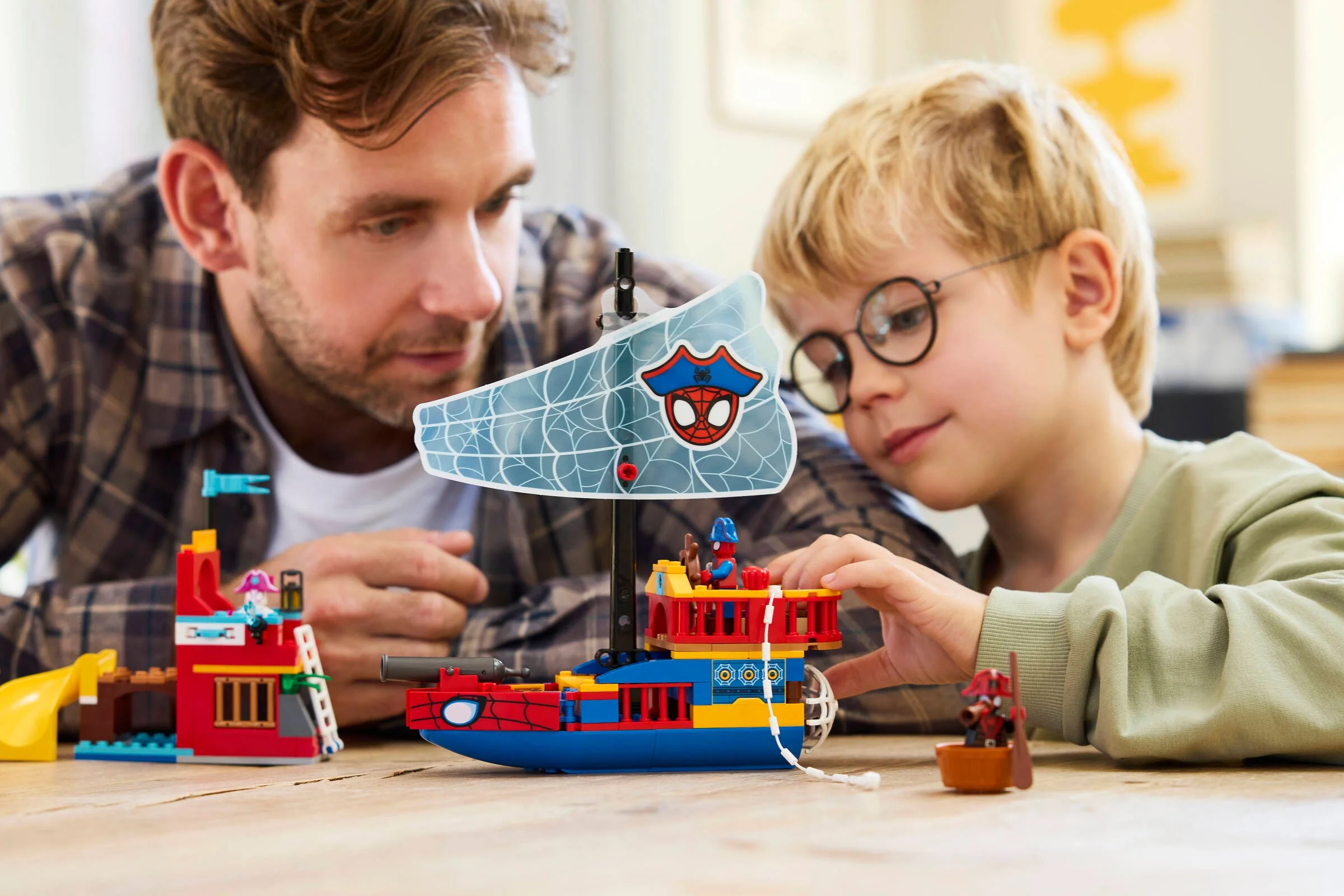 Un tată și fiul se joacă cu setul LEGO 11208 Team Spidey Pirate Ship. Atmosferă familială.