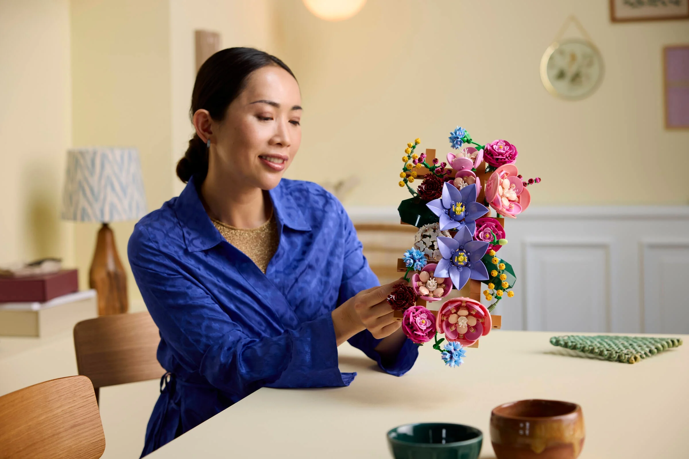 Femeie zâmbitoare asamblând setul LEGO 11503 Flower Wall, prezentând florile colorate.