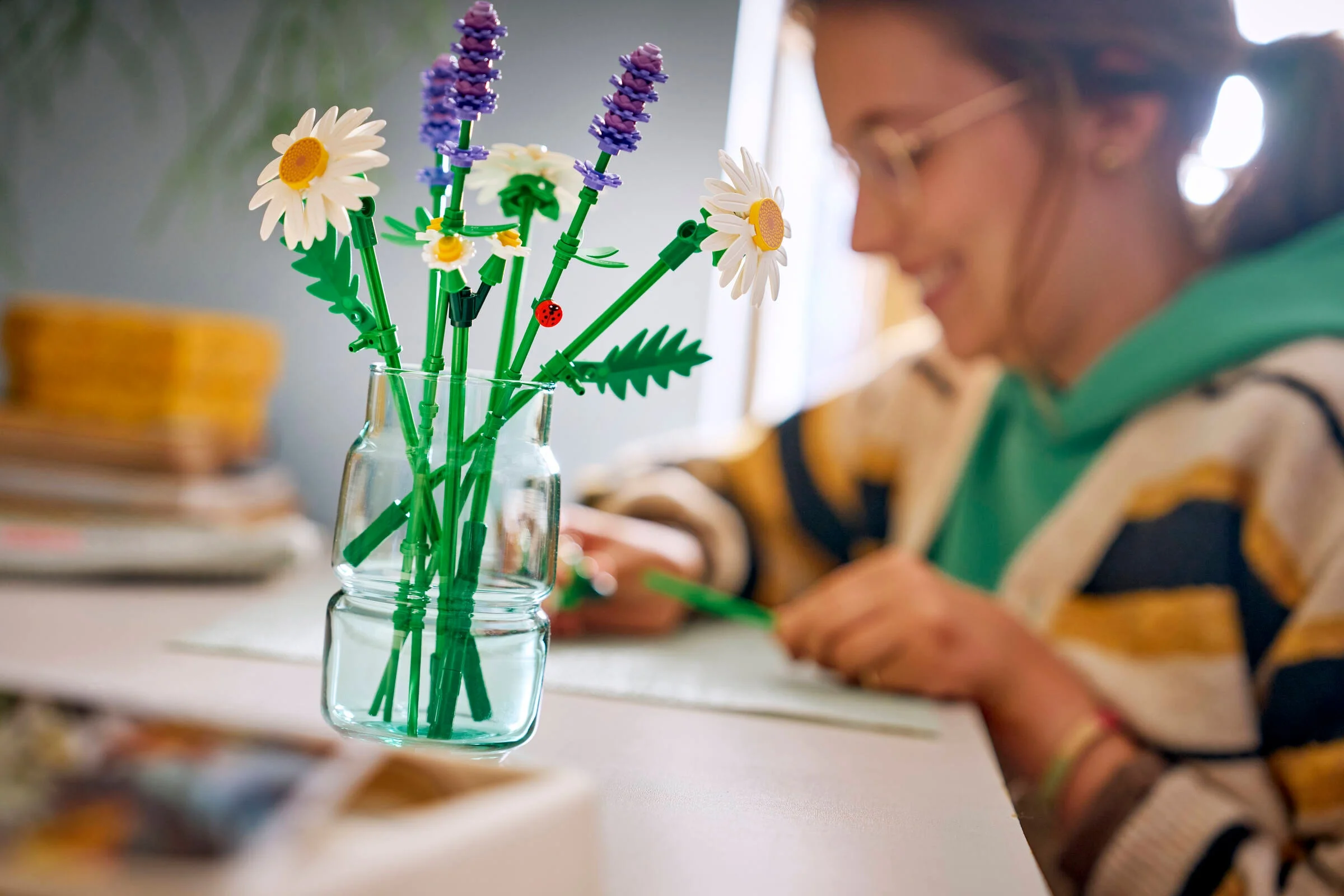Imagine cu setul LEGO 11508 Daisies într-o vază, alături de o persoană care scrie.