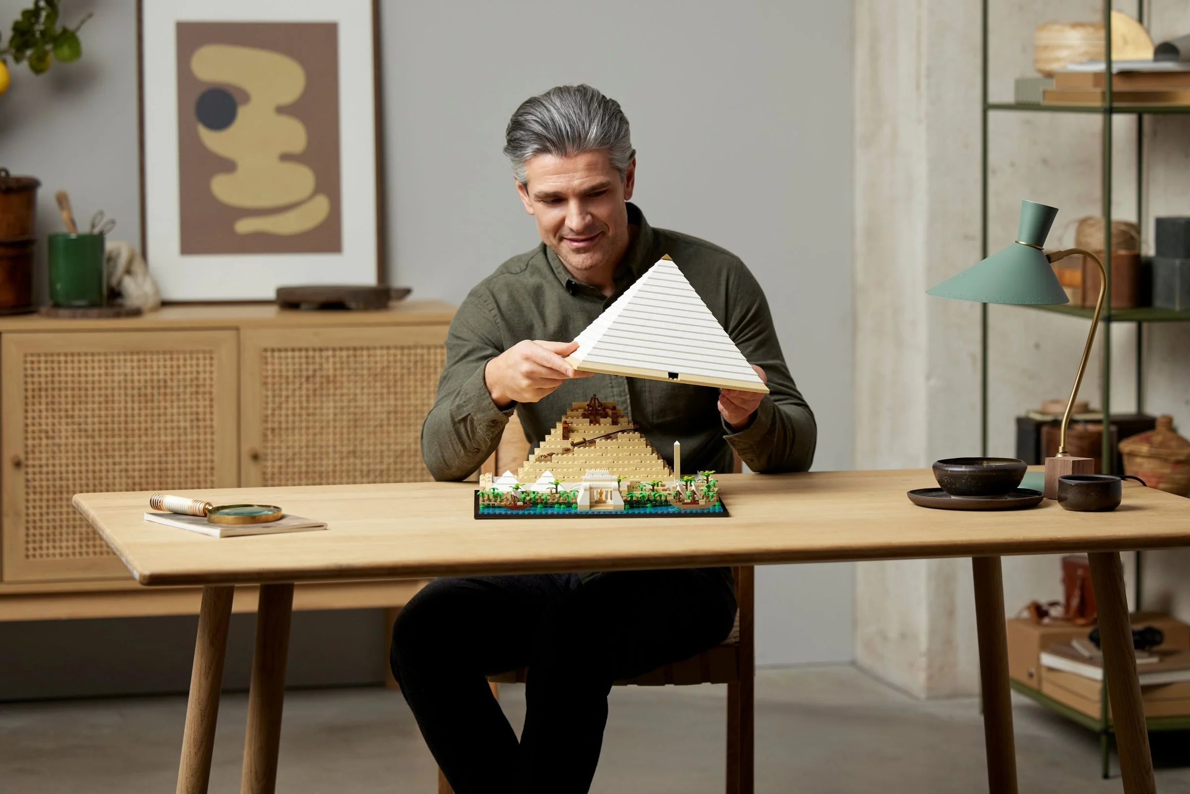 Bărbat asamblând piramida LEGO, arătând partea finisată și cea în construcție.