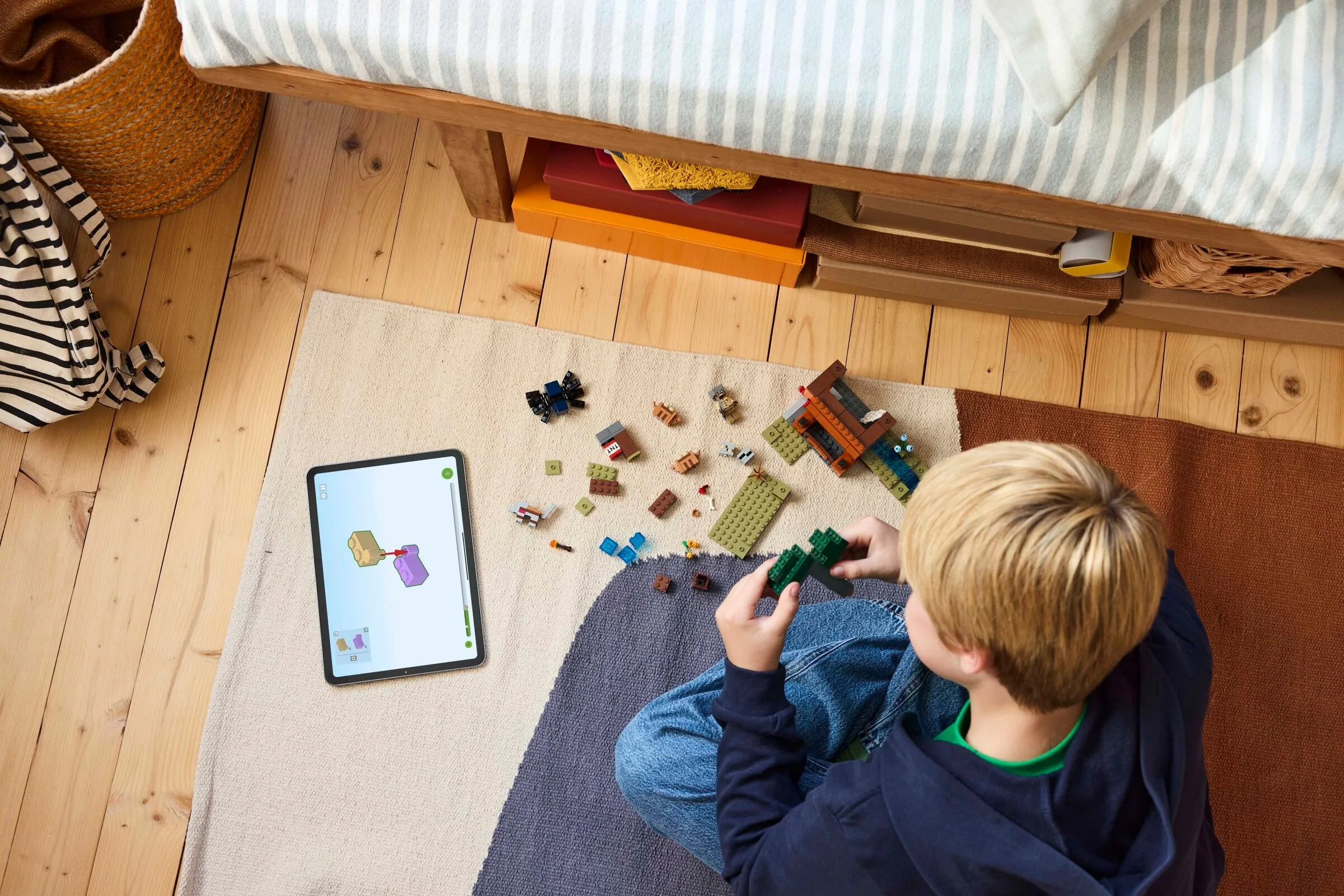 Copil asamblând setul LEGO Minecraft 21269 pe un covor, folosind instrucțiuni digitale.