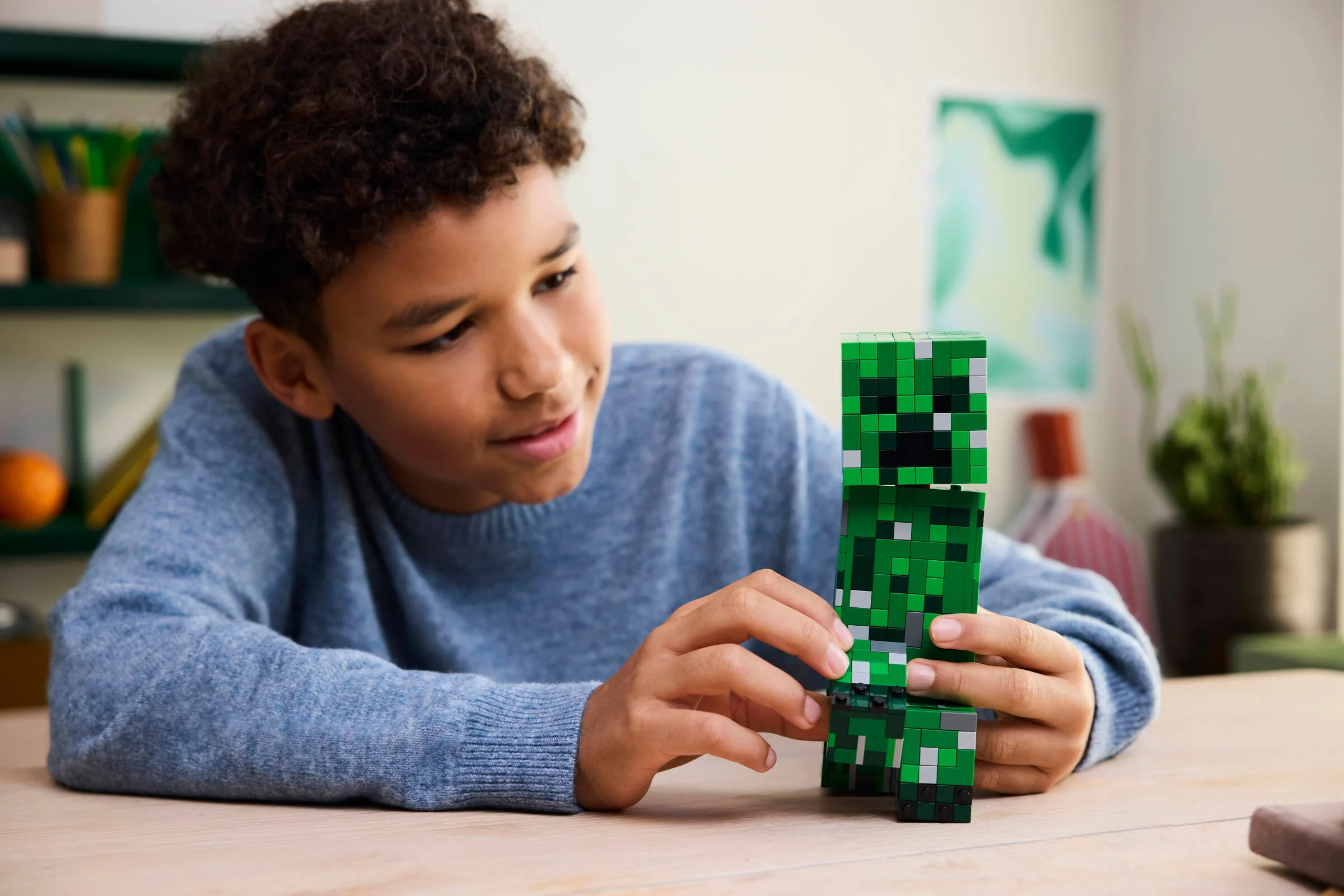 Un băiat zâmbește în timp ce ține Creeper-ul LEGO Minecraft.