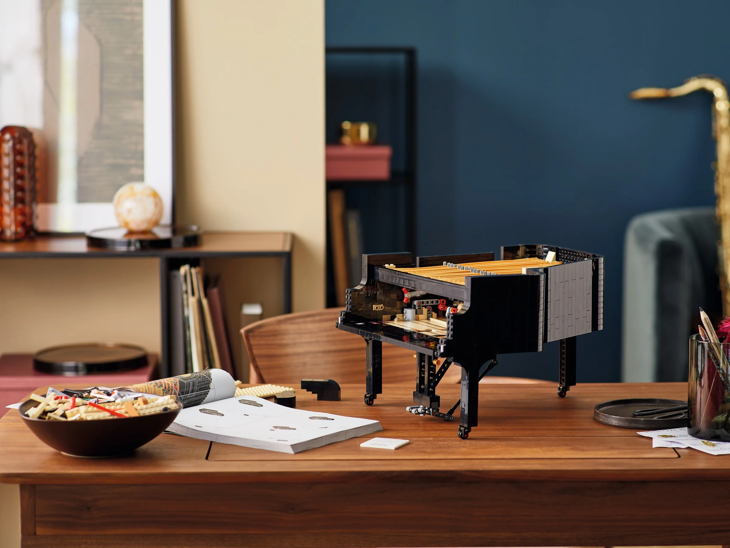 Grand Piano LEGO 21323 pe un birou, cu instrucțiuni și piese pregătite, ambient artistic.