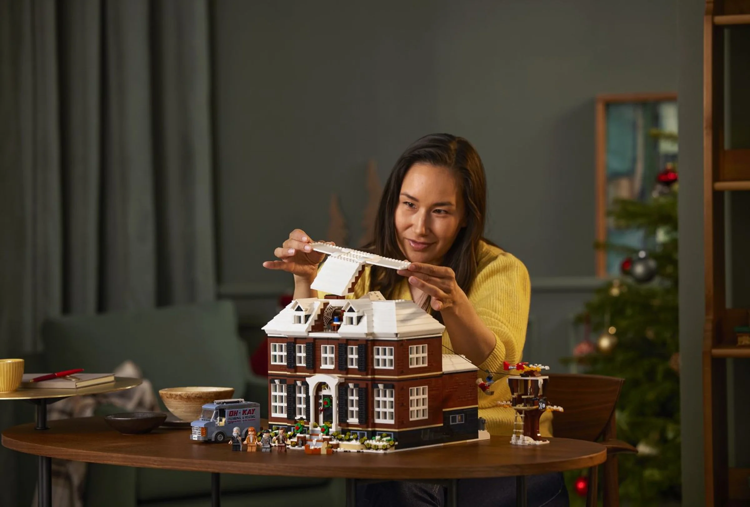 Femeie construind casa LEGO Home Alone, set 21330. Detalii vizibile ale modelului și minifigurine.