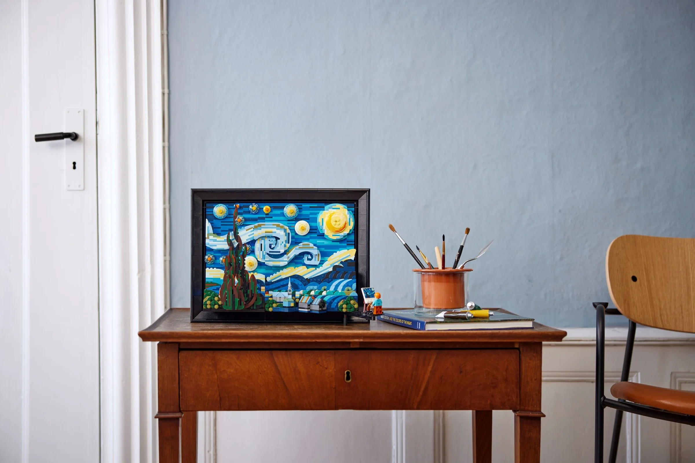 Modelul LEGO Starry Night, cu minifigurina Van Gogh, pe o masă de lemn, într-o cameră.